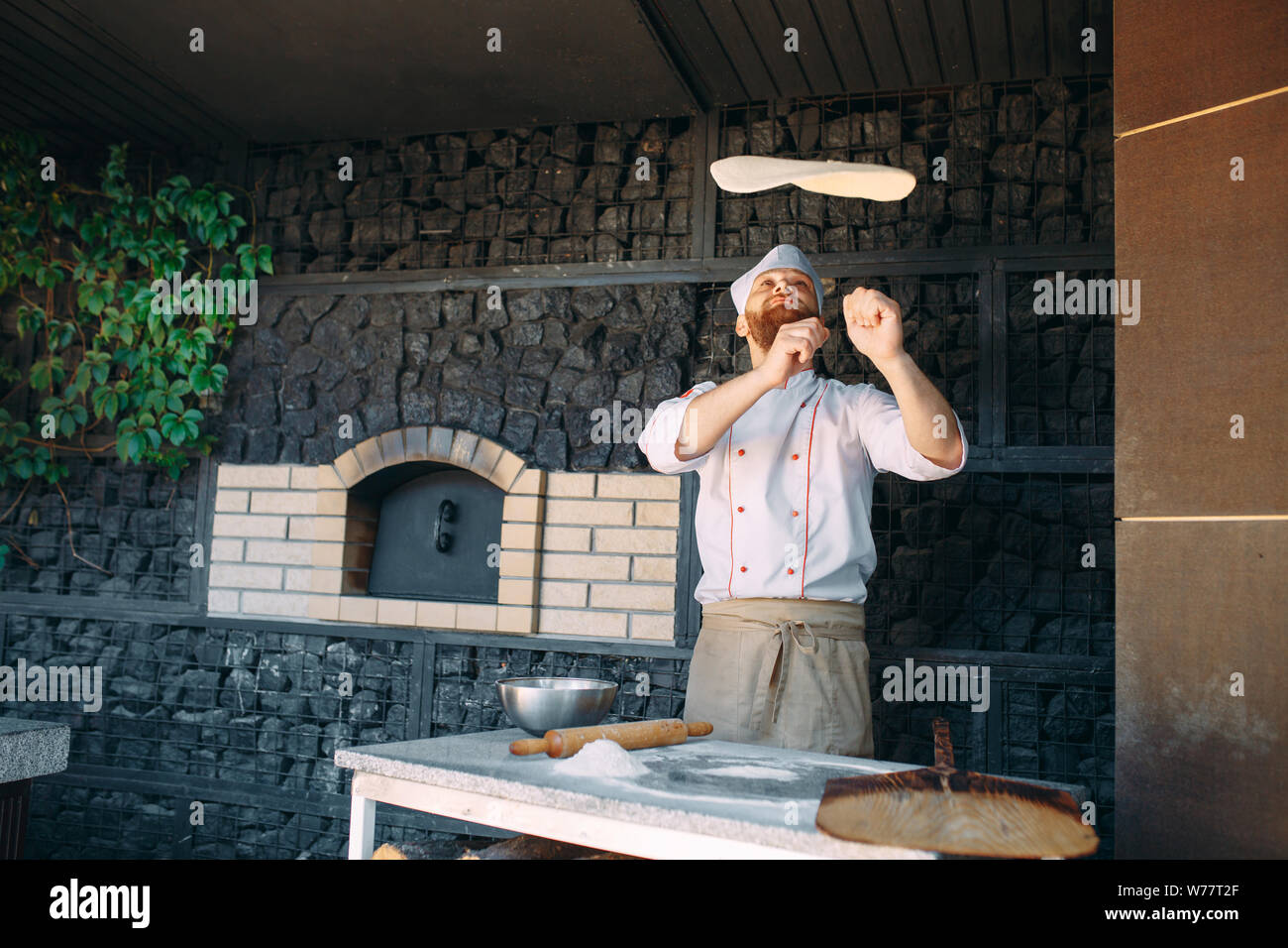 Skilled chef preparing dough for pizza rolling with hands and throwing up. Stock Photo