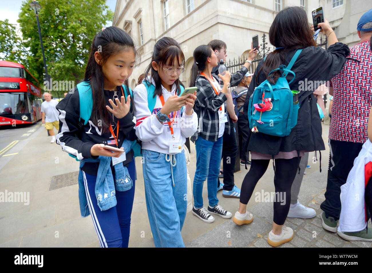 London, England, UK. Young Japanese tourists in Whitehall looking at their mobile phones Stock Photo