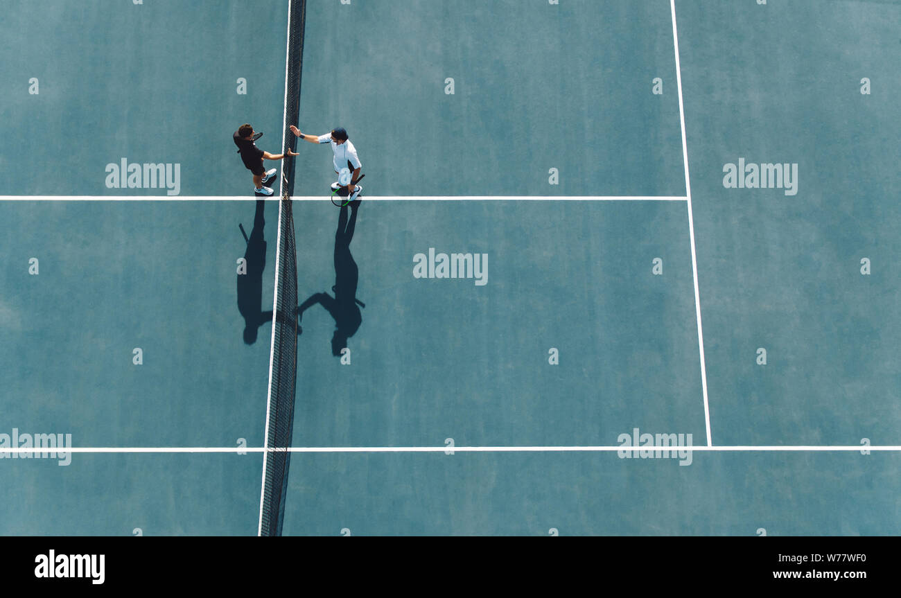 Aerial shot of professional tennis players handshakes at the net. sportsmen shaking hands over the net on hard court. Stock Photo