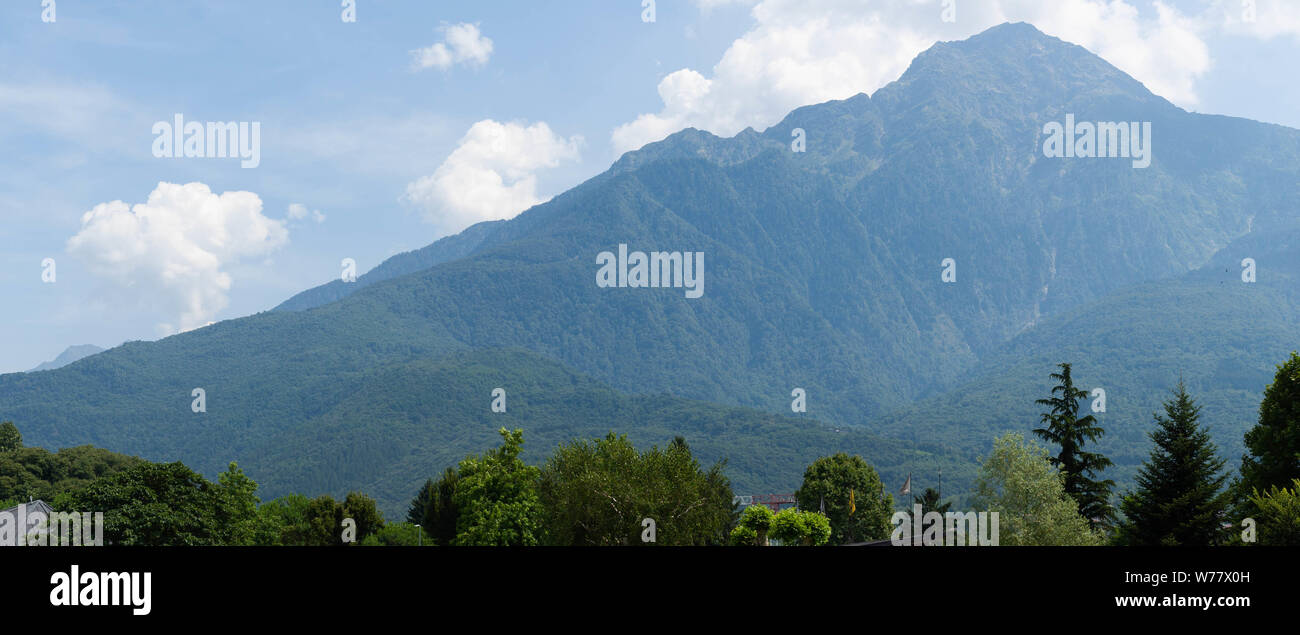Fantastic view of mountains and trees on a sunny summer day. District of Como Lake, Colico, Italy, Europe. Panoramic view. Stock Photo
