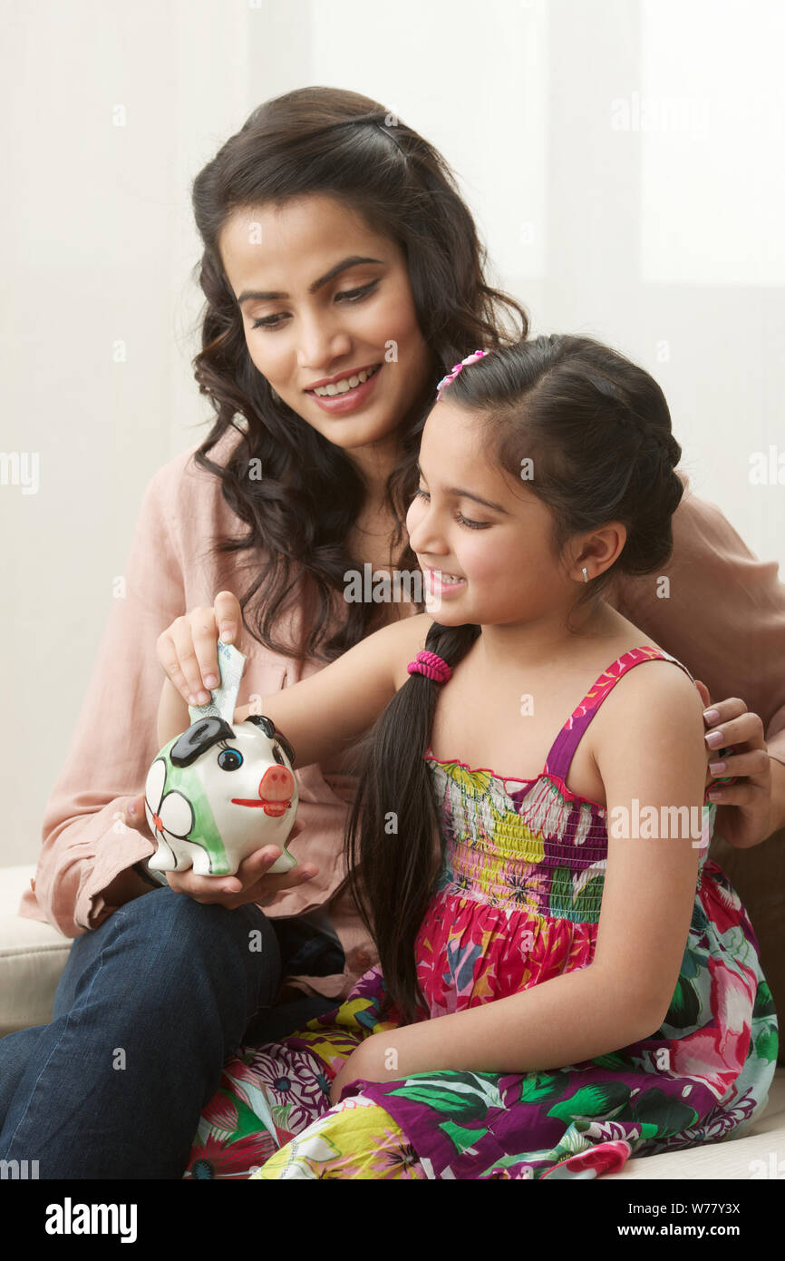 Girl putting money into a piggy bank with her mother Stock Photo - Alamy