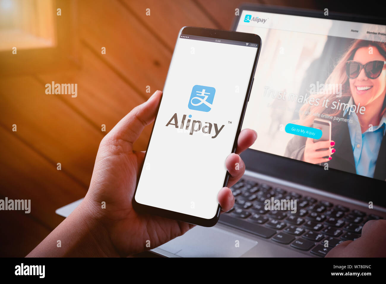 Bangkok, Thailand - August 5, 2019: Hands holding Smartphone with Alipay logo on screen and Alipay website on laptop background. Alipay is mobile and Stock Photo