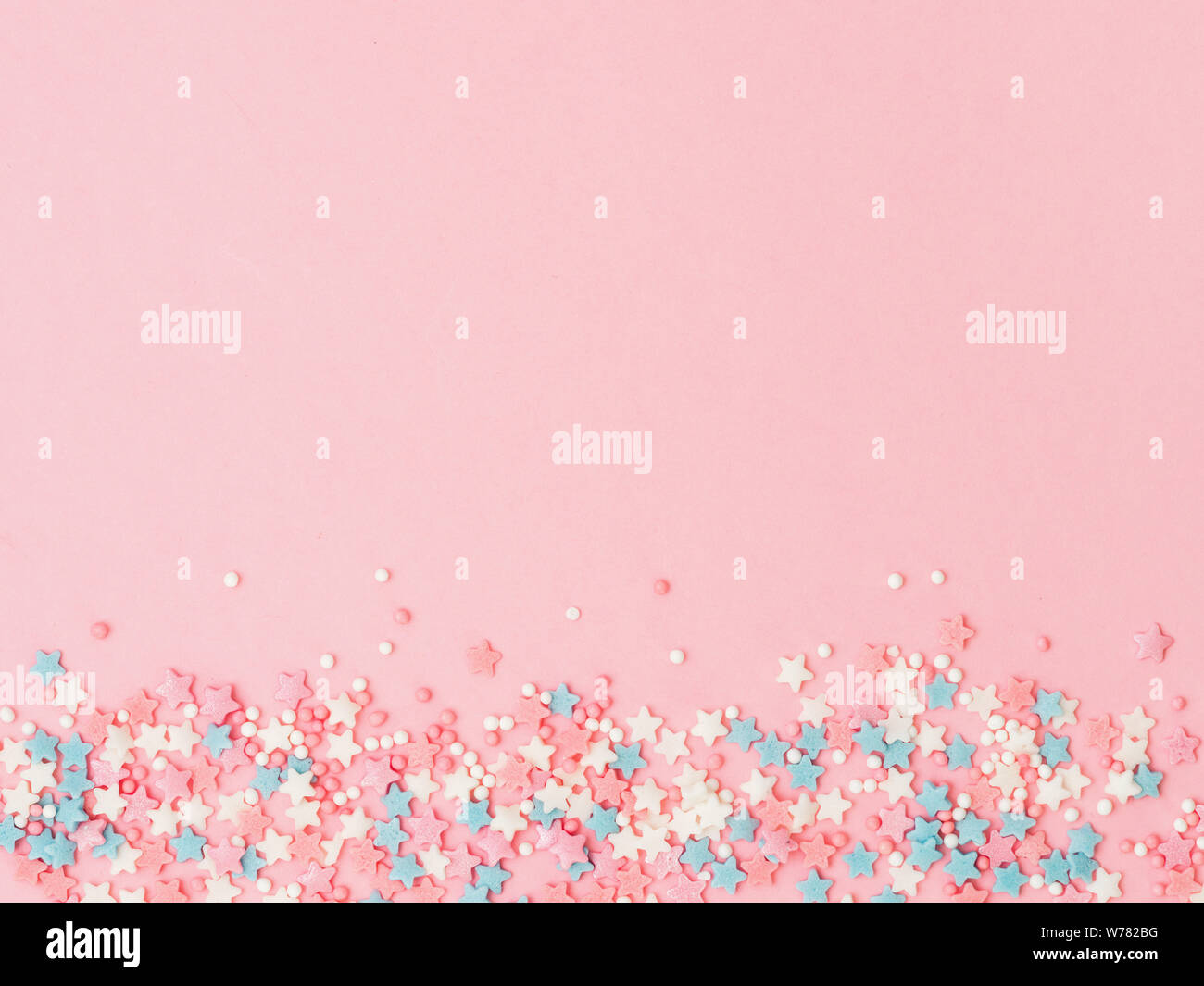 Festive border frame of colorful pastel sprinkles on pink background