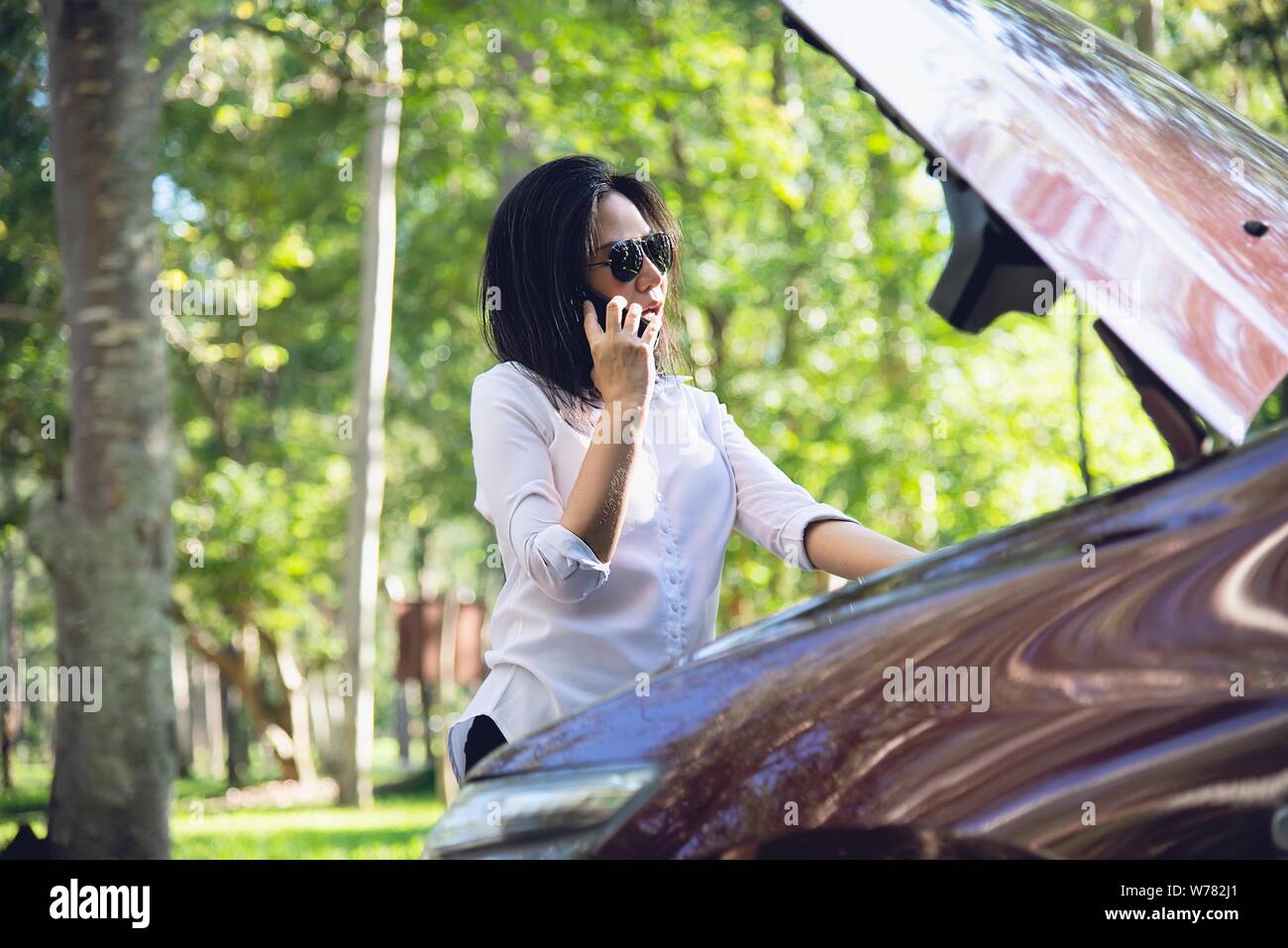 Asian woman calling repairman or insurance staff to fix a car engine problem on a local road - people with car problem transportation concept Stock Photo