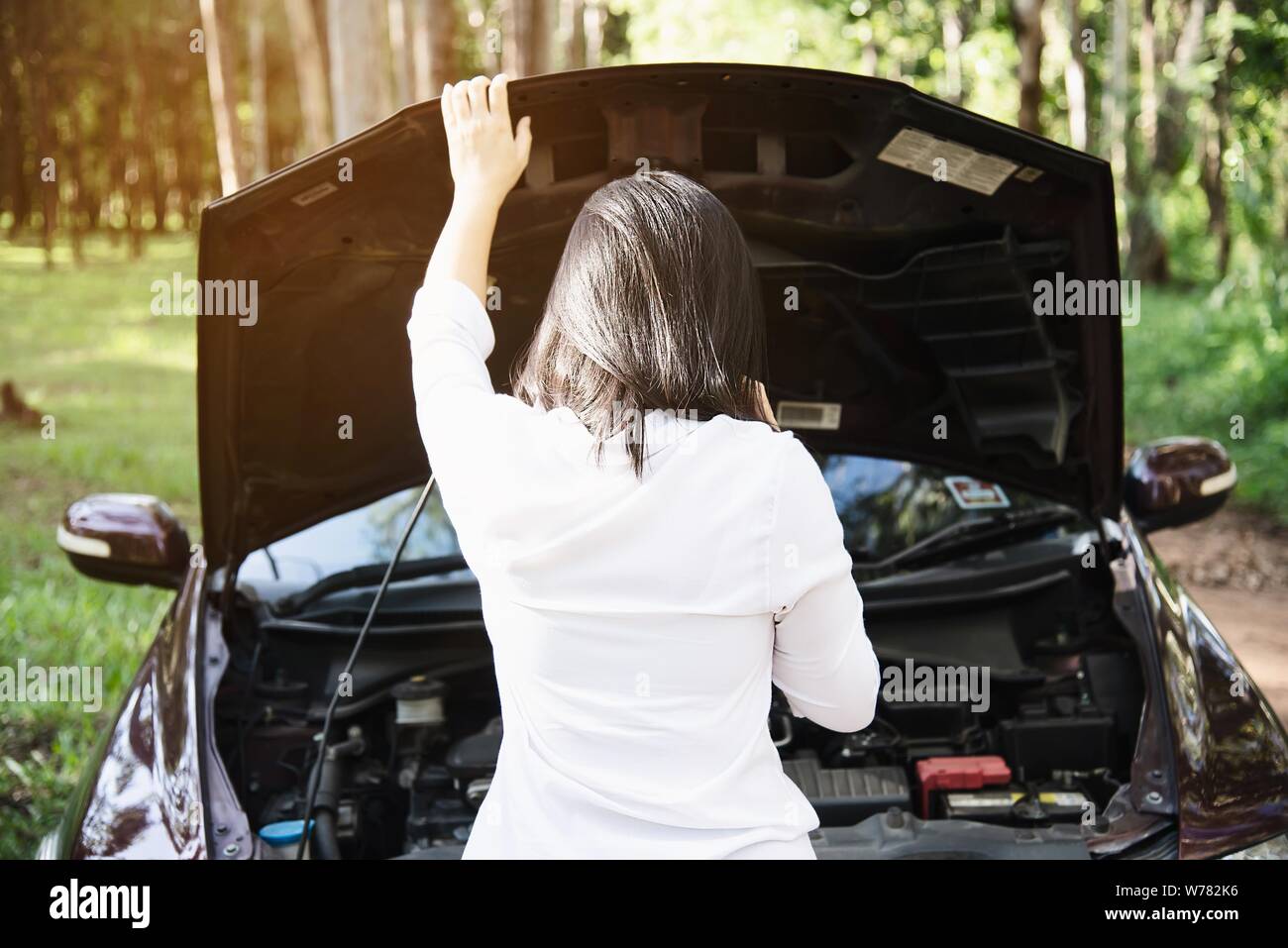 Asian woman calling repairman or insurance staff to fix a car engine problem on a local road - people with car problem transportation concept Stock Photo