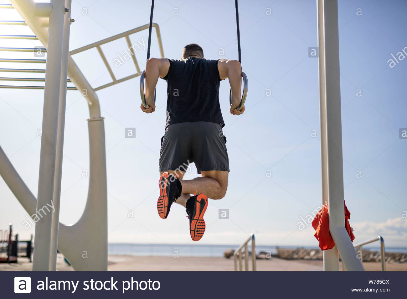 Handsome strong man hanging on gymnastics rings at outdoor ...