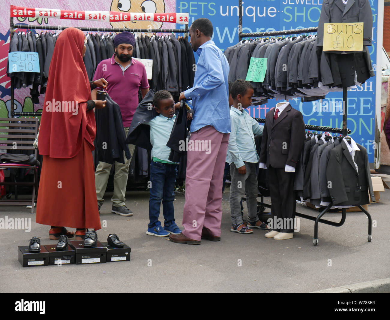 Family out shopping for boys suits on an outdoor market in England UK, one boy tries on a jacket while parents negotiate a price.  photo DON TONGE Stock Photo