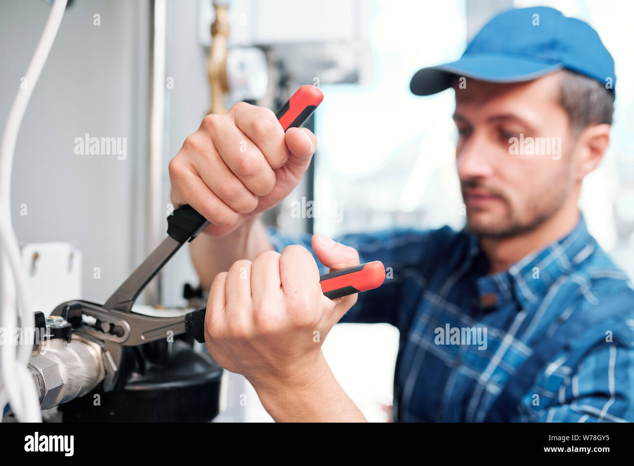 Hands of young contemporary technician with pliers fixing nut on pipe Stock Photo