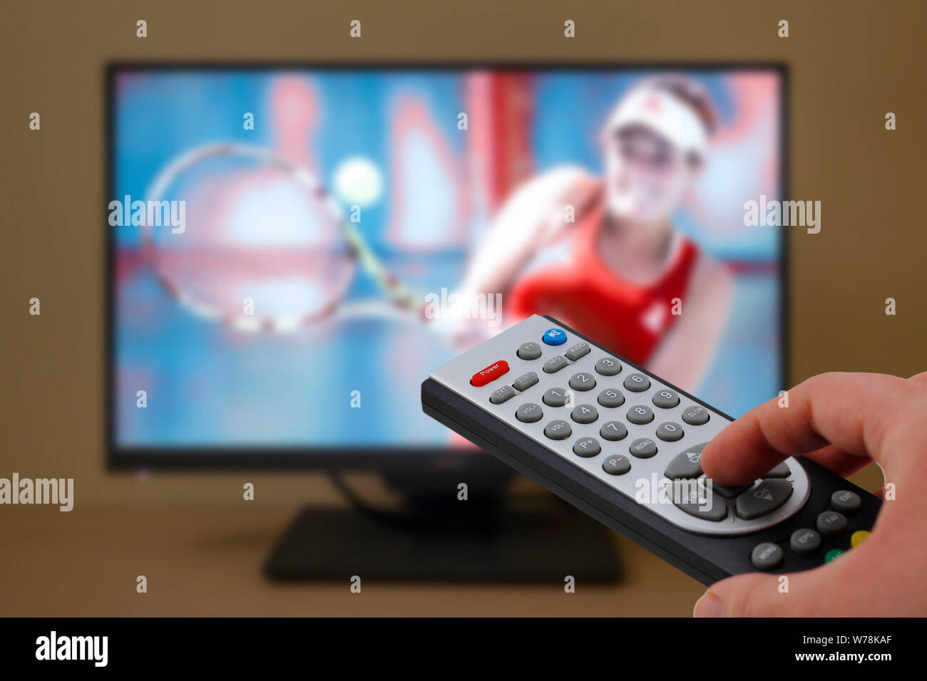 Watching a tennis match in the television, with a tv remote control in the hand Stock Photo