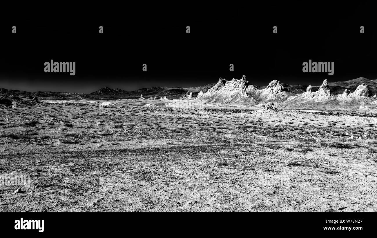 Cold dark barren desert landscape with jagged mountain peaks beyond under black sky. Stock Photo