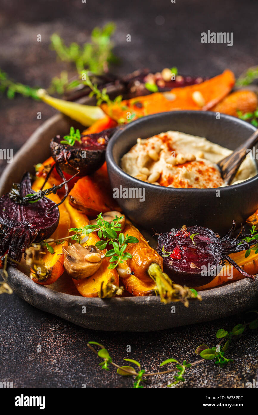 Baked carrots, beets, zucchini and yam with hummus in a dark dish Stock
