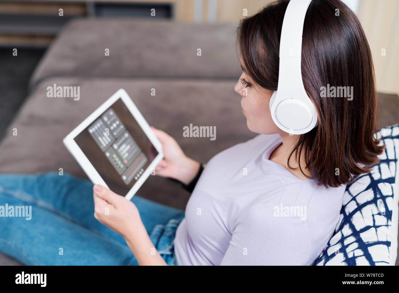 Young woman in headphones looking at remote control panel on display of touchpad Stock Photo