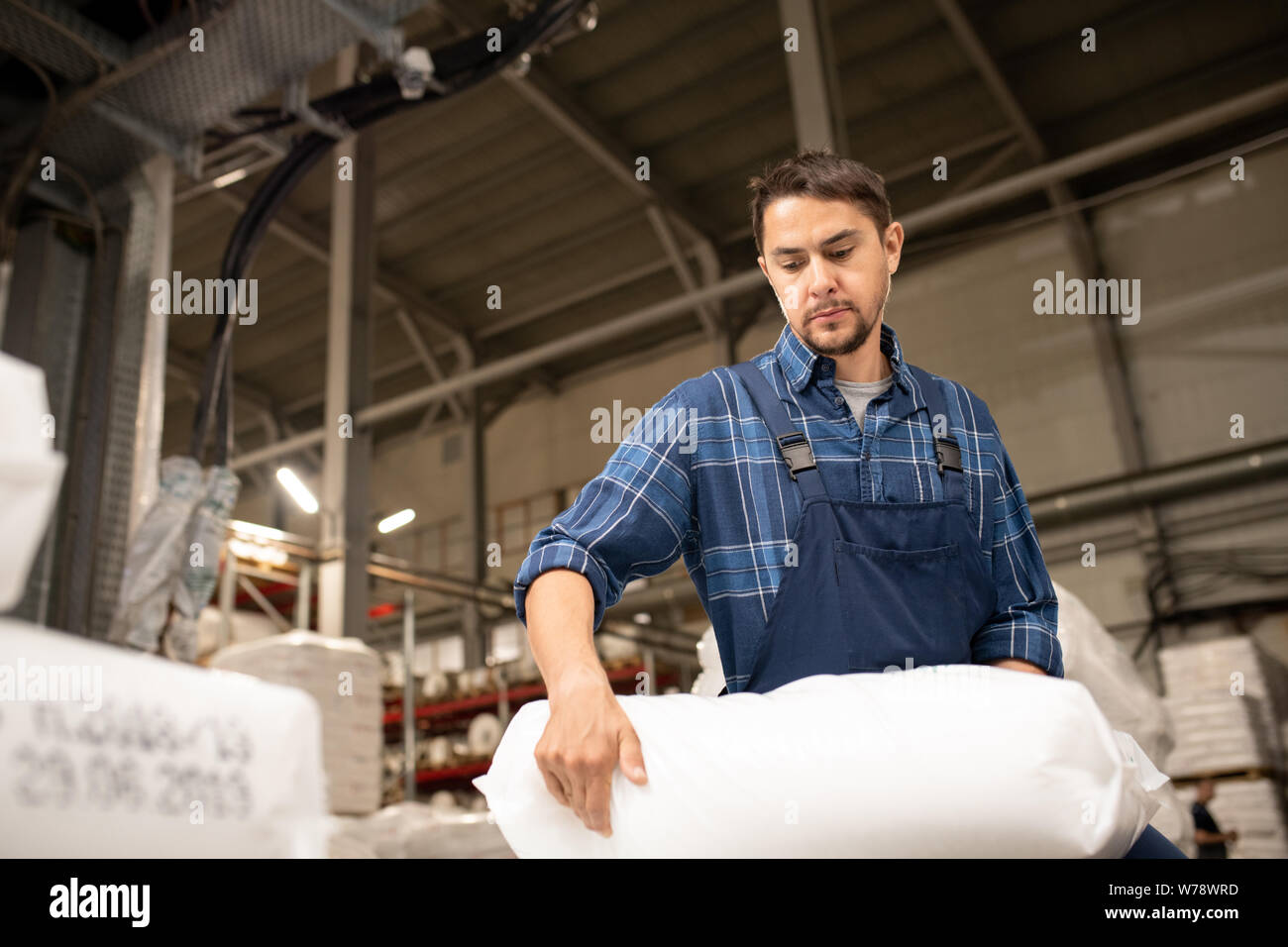 Young male worker of large polymer production factory loading sacks Stock Photo