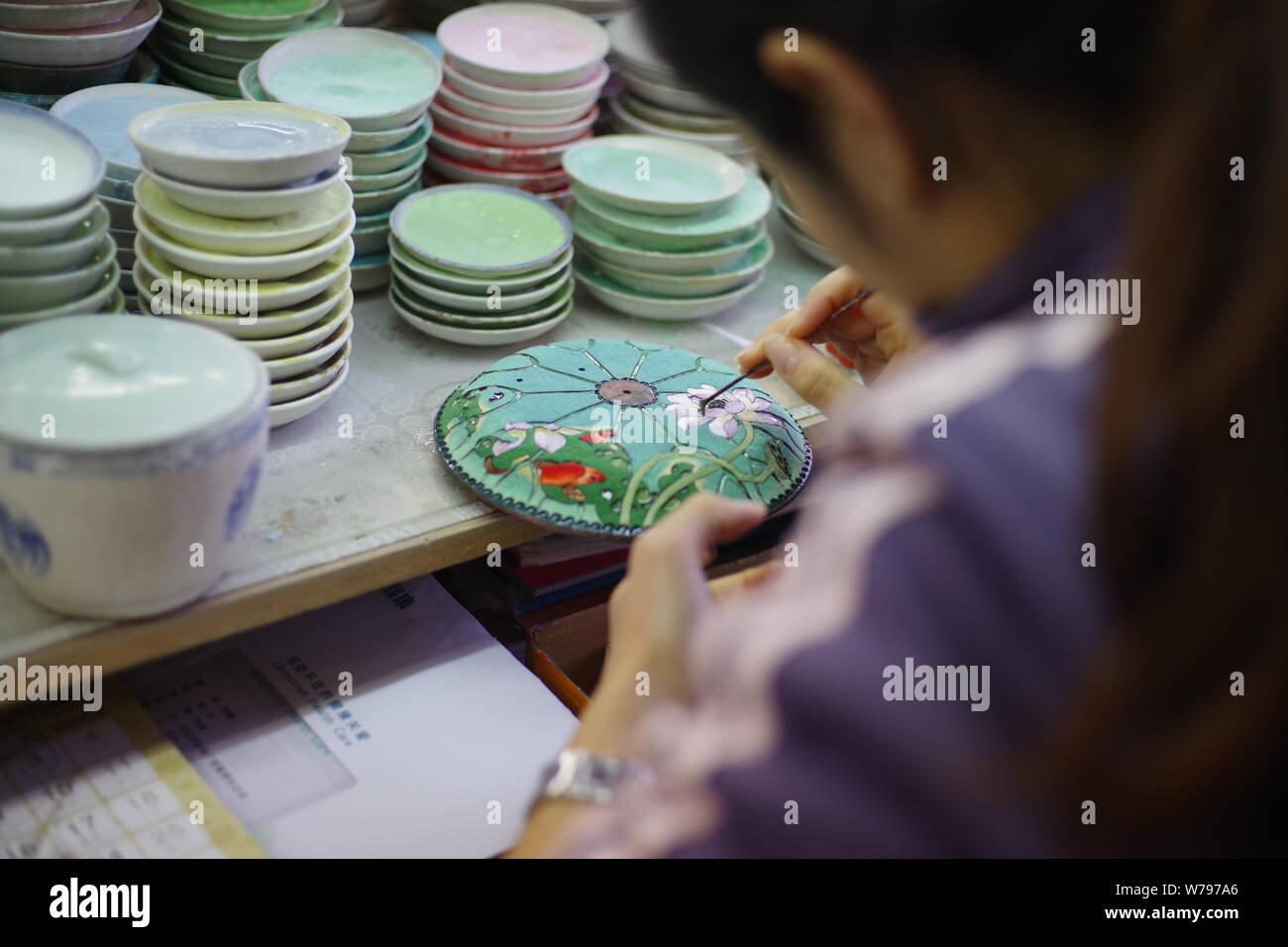 A Chinese worker adds cloisons according to the pattern previously transferred to the workpiece in the biggest cloisonne factory, Beijing Enamel Facto Stock Photo