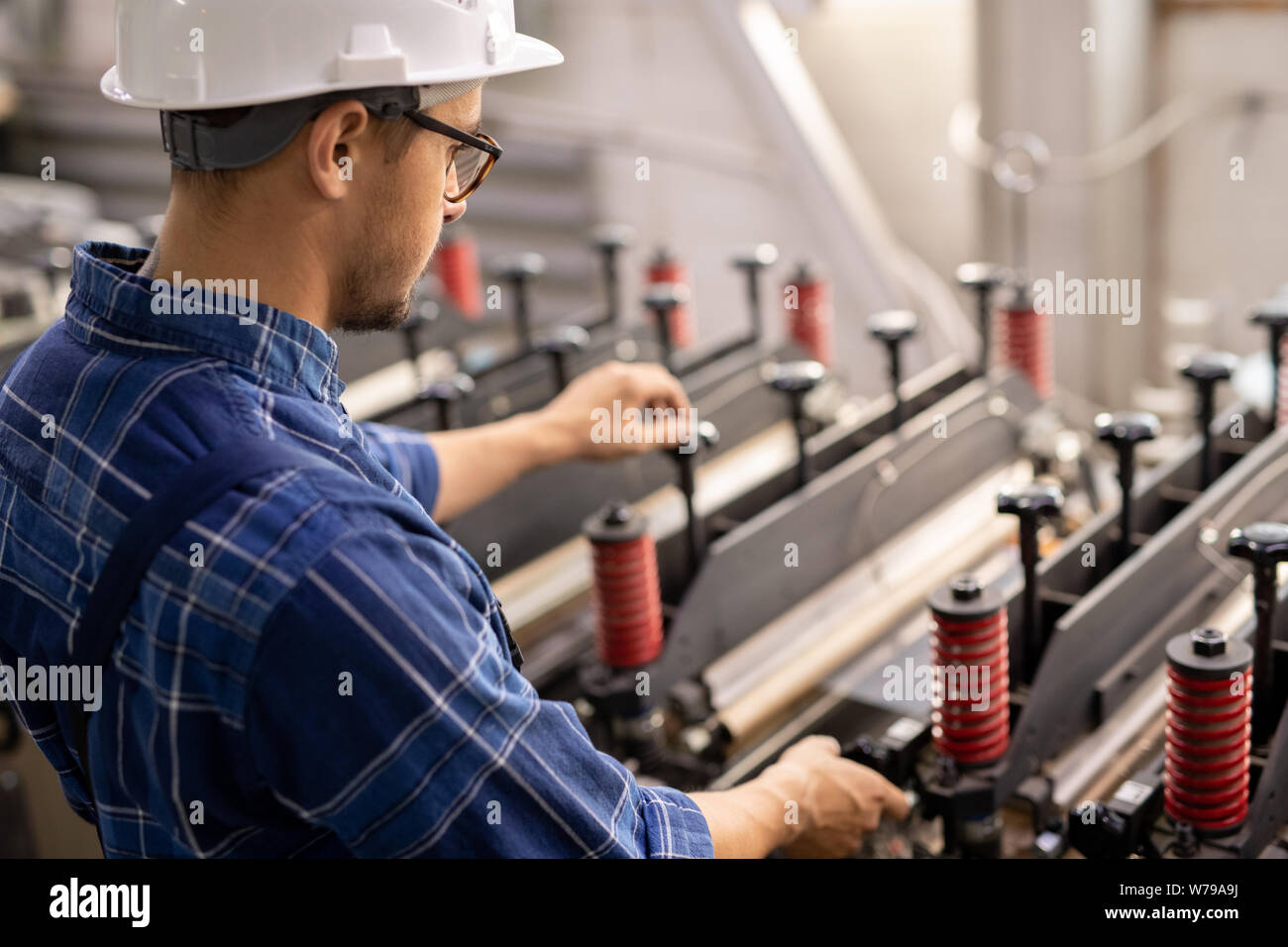 Young engineer standing by industrial machine while operating it in working area Stock Photo