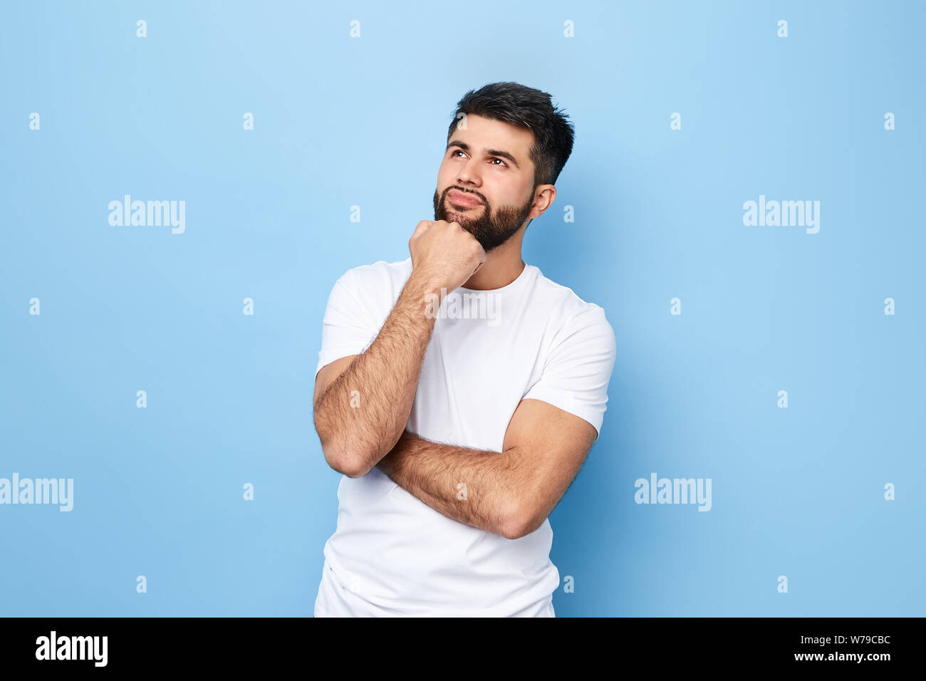 thoughtful dreaming romantic man touching his chin and weighs the pluses and minuses of the offer isolated on blue background with copy space for text Stock Photo