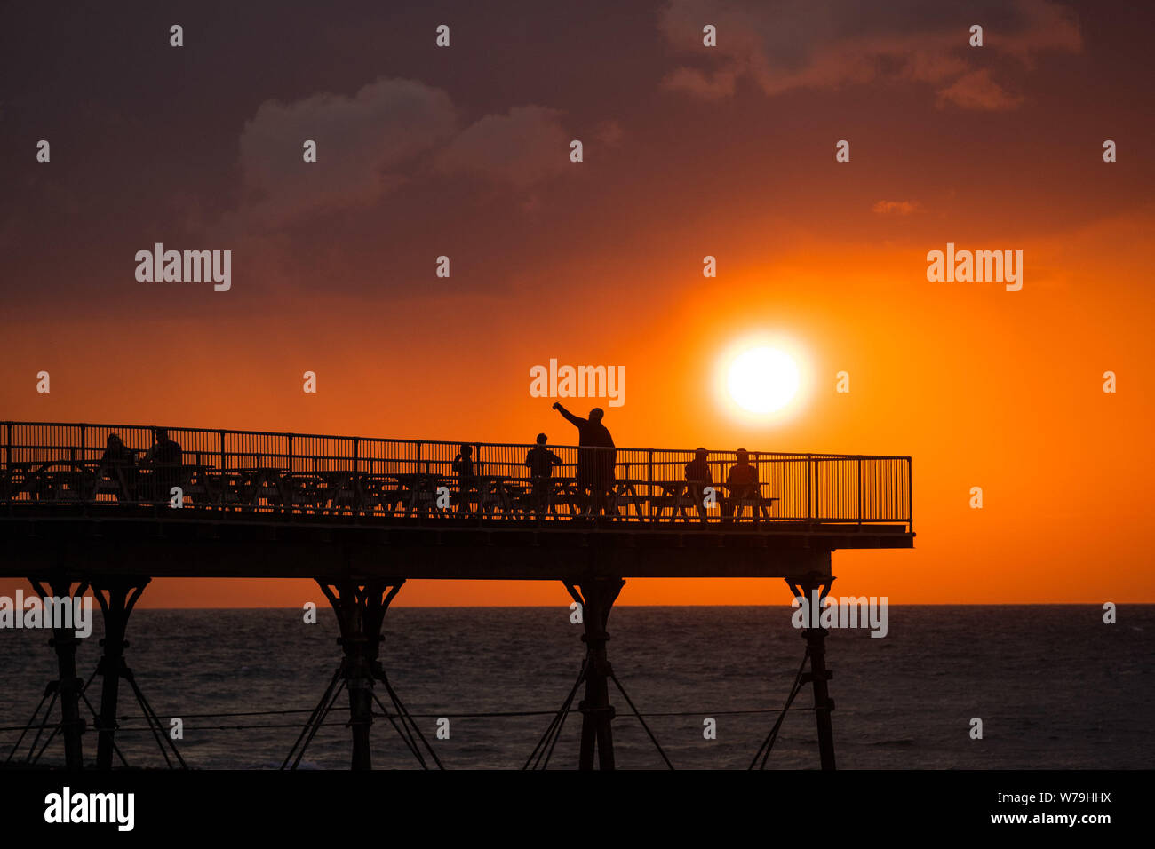 Aberystwyth, Wales, UK. 5th Aug 2019.  People on the Royal Pier in Aberystwyth are silhouetted as they watch the fiery sunset at the end of a breezy but bright August day. The weather is forecast to become more unsettled towards the weekend, with outbreaks of rain in many places  Photo credit : Keith Morris/Alamy Live News Stock Photo