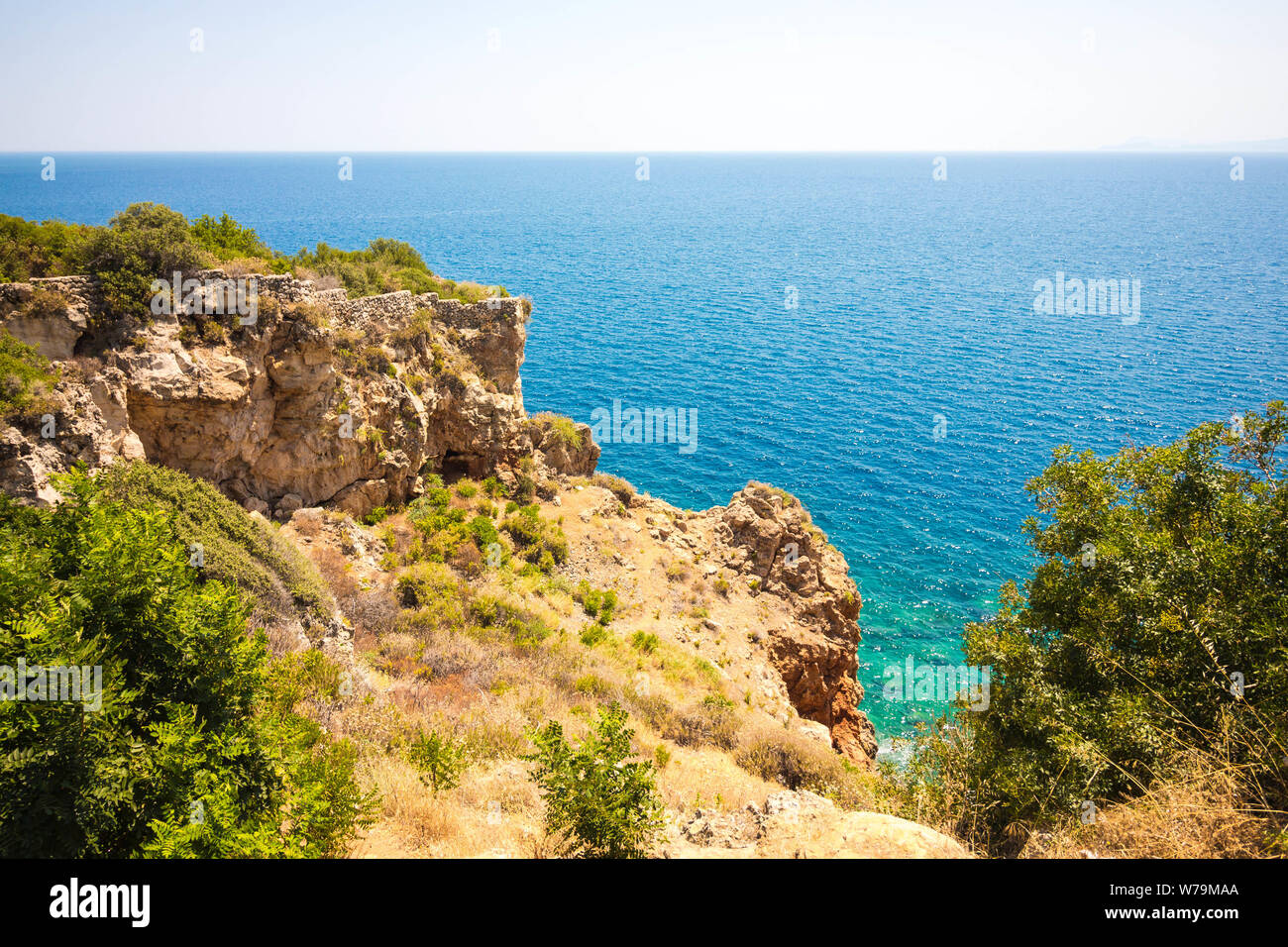 Beautiful view from the cliff of the sea. The water is clear with a blue tint. Bushes and various vegetation grow on the rock. Stock Photo