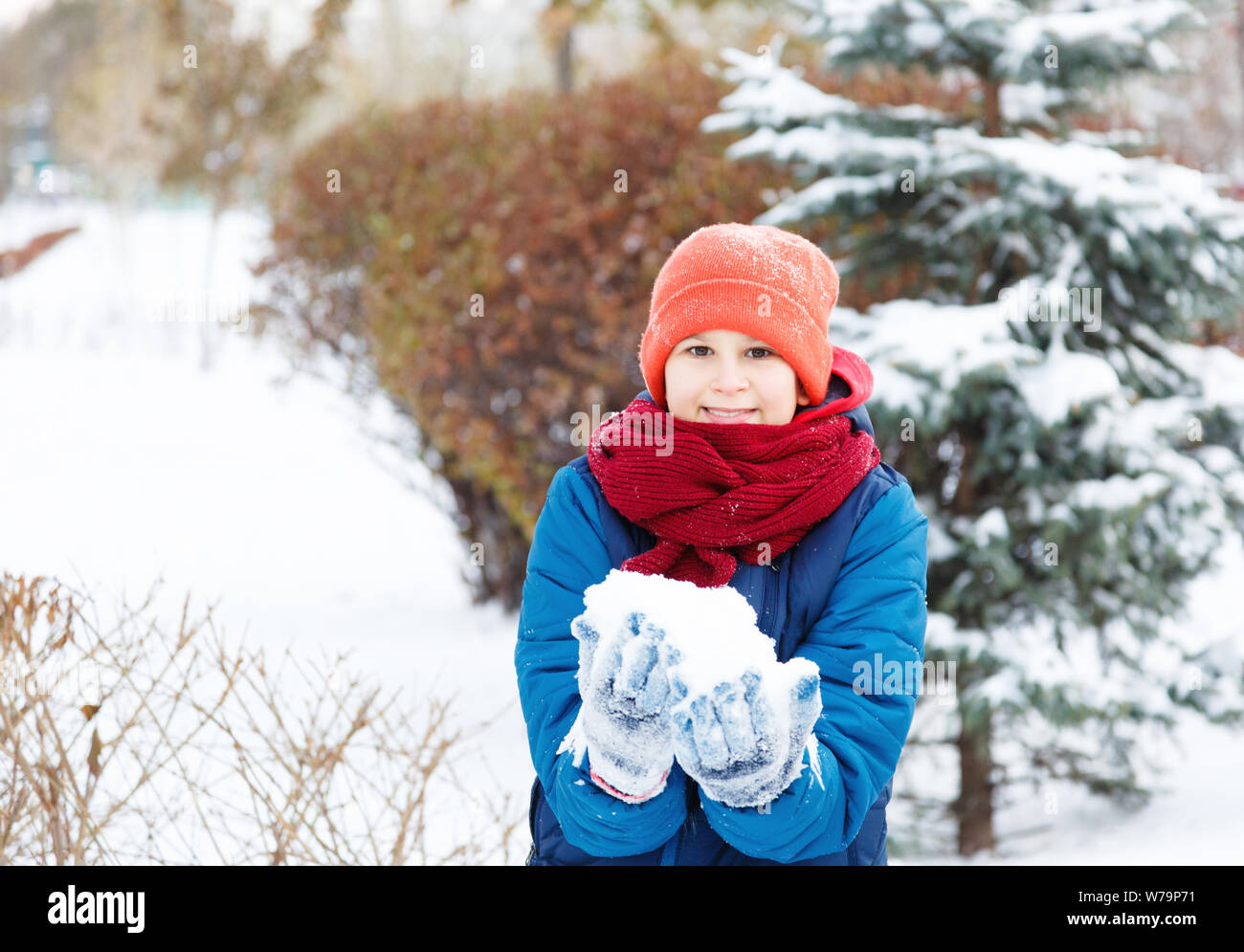 Happy cute excited boy teenager plays with snow, makes snowballs. Winter activity, active leisure and entertainment concept. Stock Photo