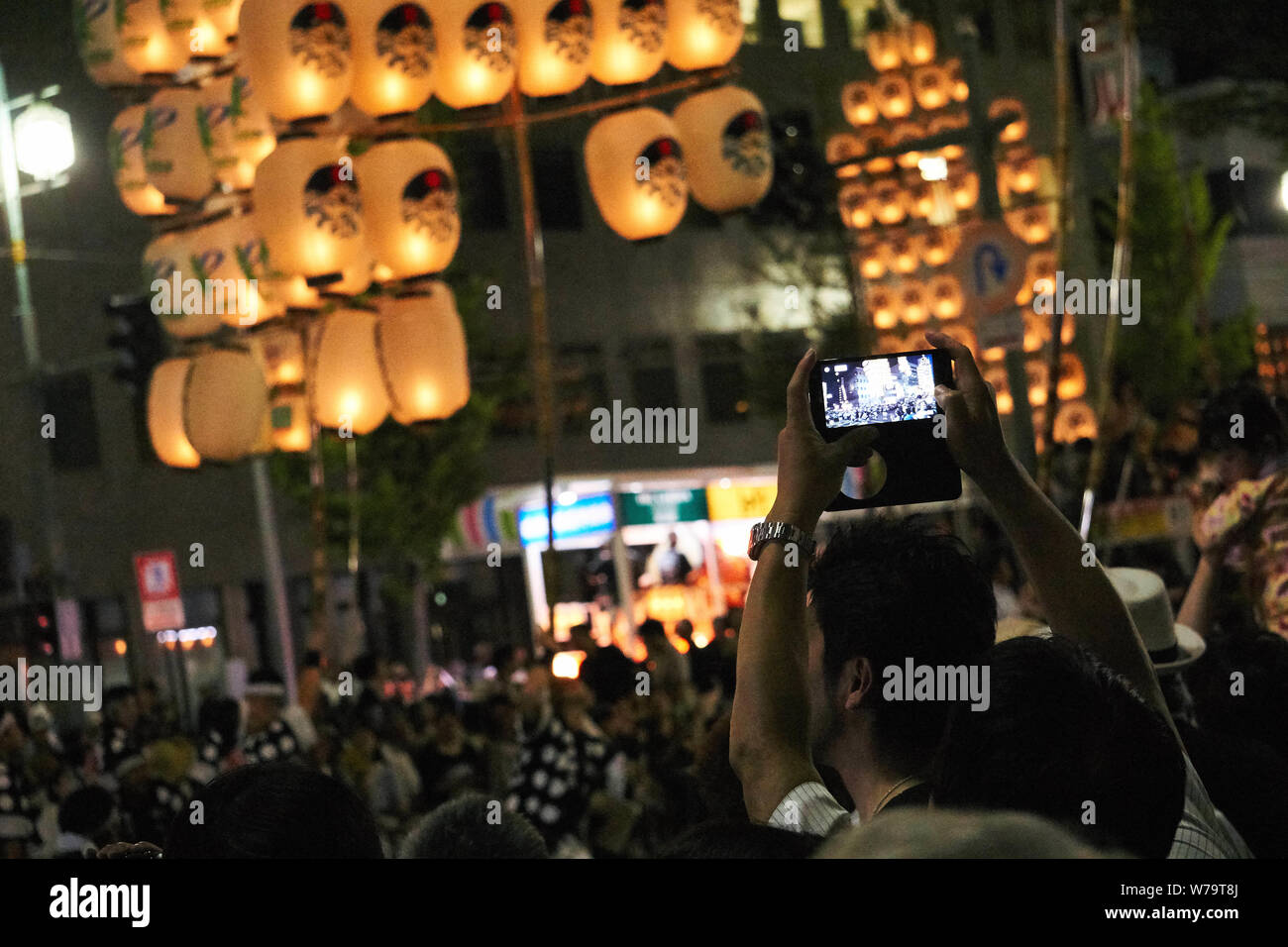 A man takes a smartphone photo as traditional candlelit Japanese lanterns are raised on bamboo poles and paraded at the Akita Kanto Matsuri Festival. Stock Photo