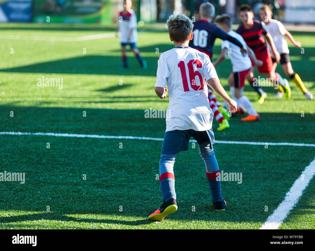 Boys in red and blue sportswear plays football on field, dribbles ball