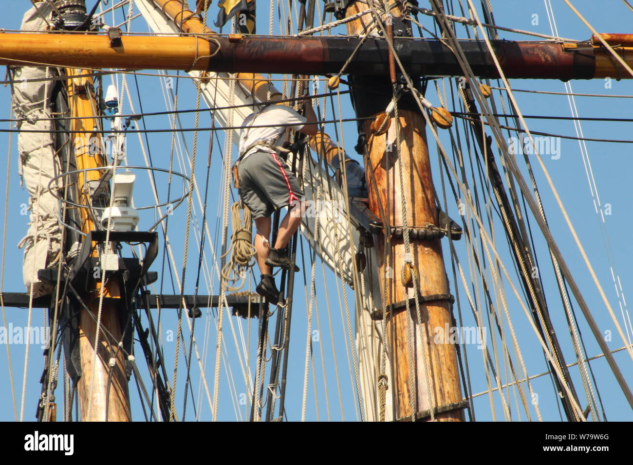 A male crew member of the Pride of Baltimore II climbs the rigging to fix part of the Tall Ship's mast. Stock Photo