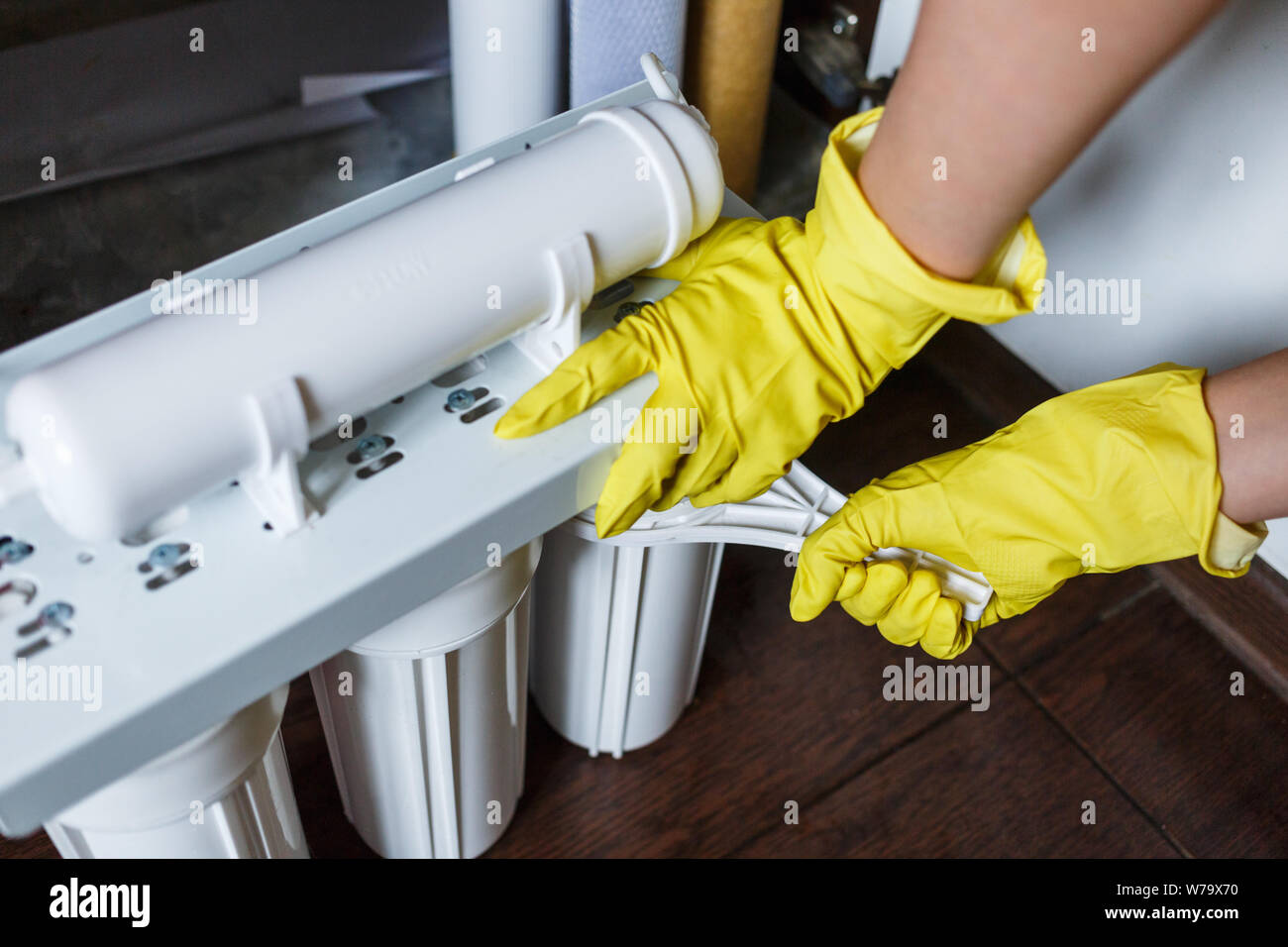 Plumber in yellow household gloves changes water filters. Repairman installing water filter cartridges in kitchen. Drinkable water filtration system i Stock Photo