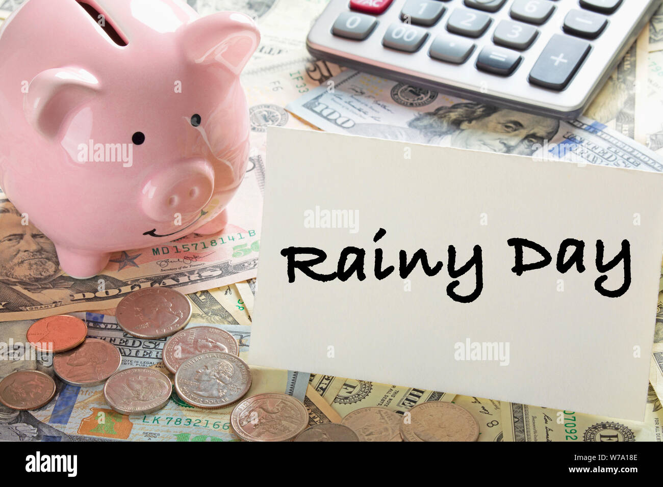 United States bank notes and coins with a calcultor, piggy bank, and a card saying Rainy Day Stock Photo