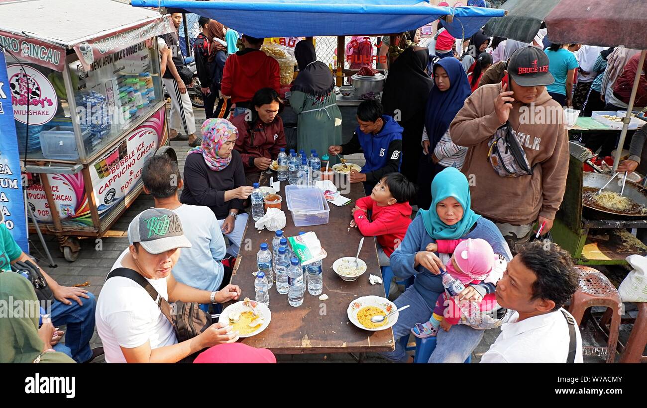 Jakarta, Indonesia - August 2019 : A group of people eat on a tabel in front of street food booths. Stock Photo