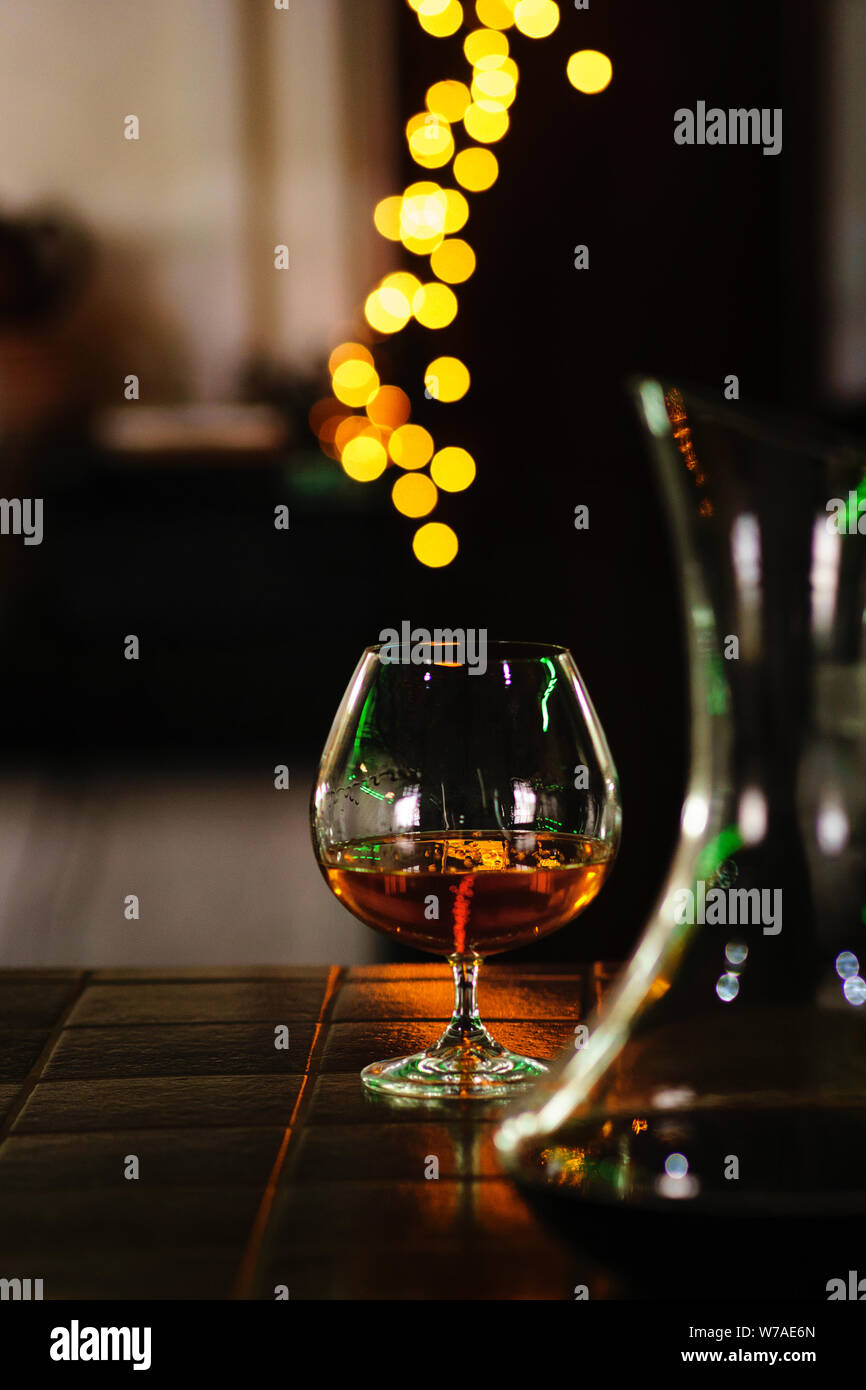 Snifter of brandy in elegant glass with space for text on dark colorful background. Decanter defocussed. Traditional French drink. Stiff drink. Servic Stock Photo