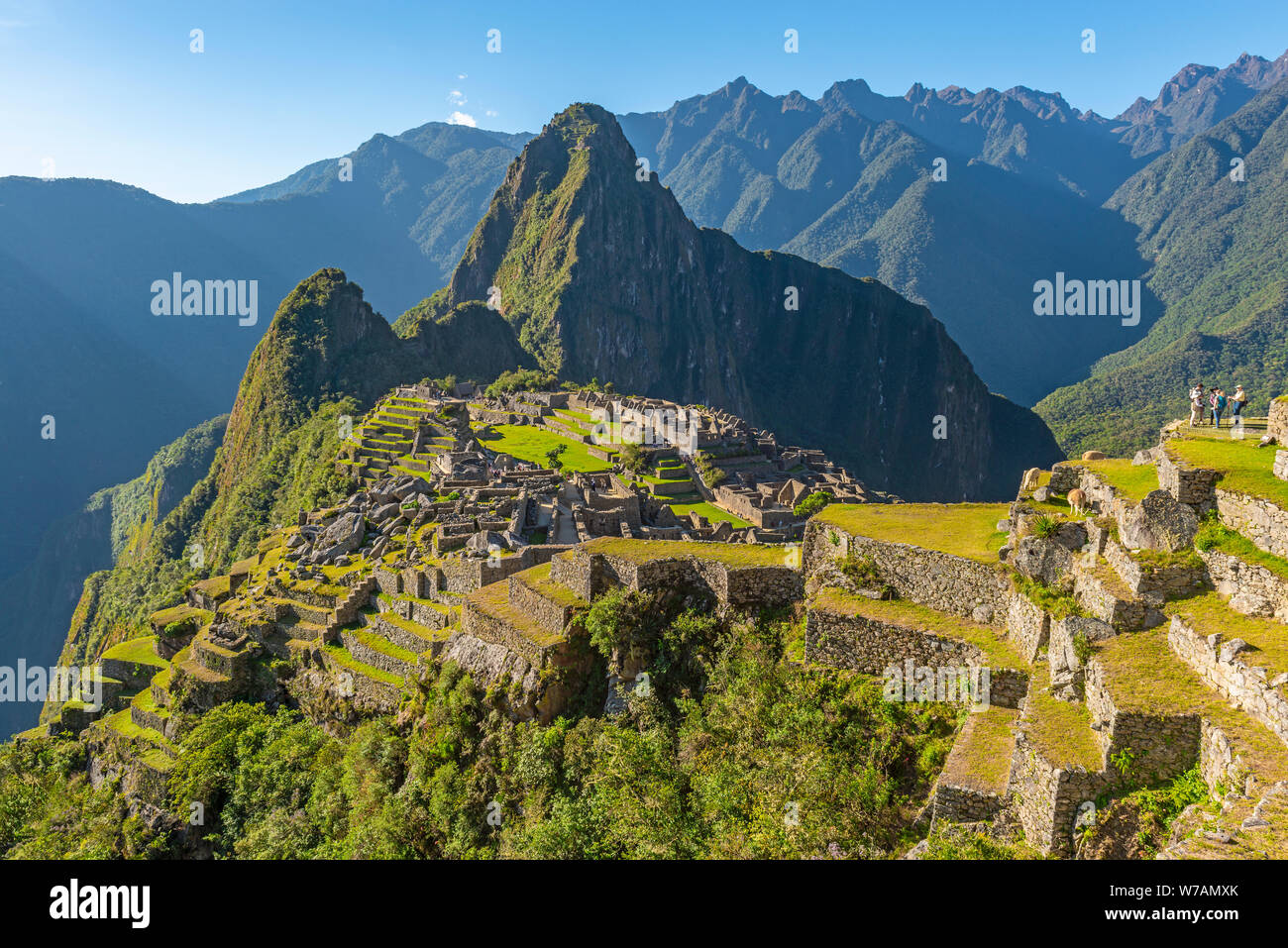 A few tourists enjoying the view from the agriculture terraces over the lost inca ruin of Machu Picchu at sunset, Cusco, Peru. Stock Photo