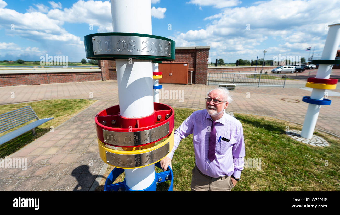 Hitzacker, Germany. 01st July, 2019. Peter Wieczorek, hotelier and chairman of the local tourism association, stands next to a column near the Elbe in Hitzacker, where the water levels of the floods of 2013 (green), 2006 (red), 2002 (yellow) and 2003 (blue) can be seen. The old town lies on the Elbe, framed by two arms of the small Jeetzel, which repeatedly led to flooding during floods. Credit: Philipp Schulze/dpa/Alamy Live News Stock Photo
