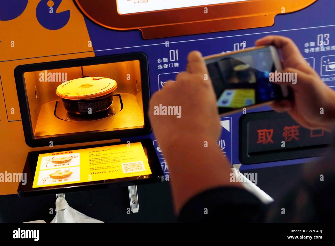 A customer takes photos of a bowl of noodle made by a mobile self-service noodle vending machine of Yo-Kai Express at an office building in Shanghai, Stock Photo