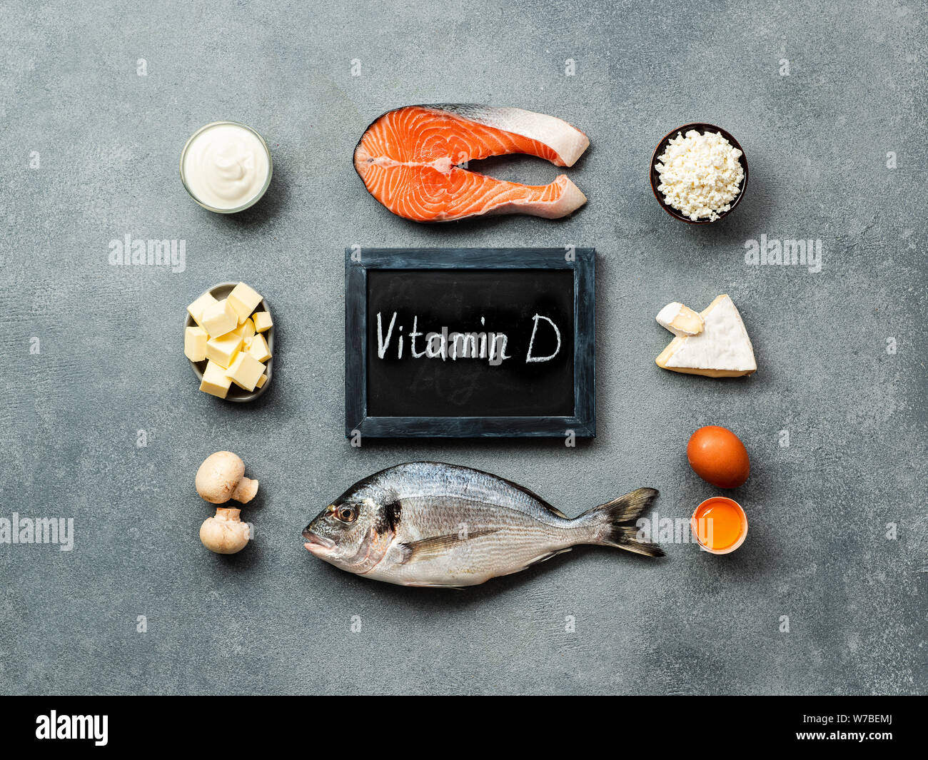 Vaitamin D sources concept. Fish, salmon, dairy products, eggs, mushrooms and chalkboard with Vitamin D words on gray stone background. Top view or flat lay. Stock Photo