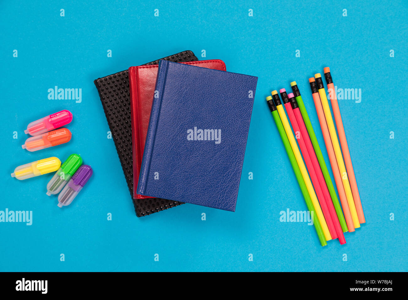 Colorful textliners and crayons and three dayplanners in leather covers are lying on pale-blue surface isolated Stock Photo