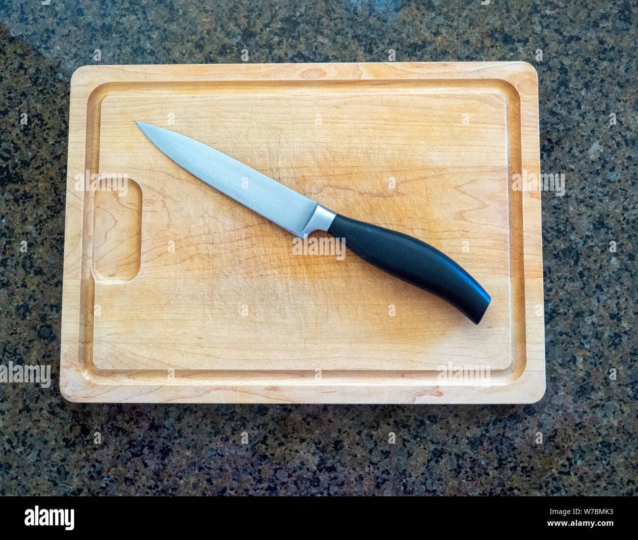 Isolated paring knife on a large wooden cutting board with a granite kitchen counter top