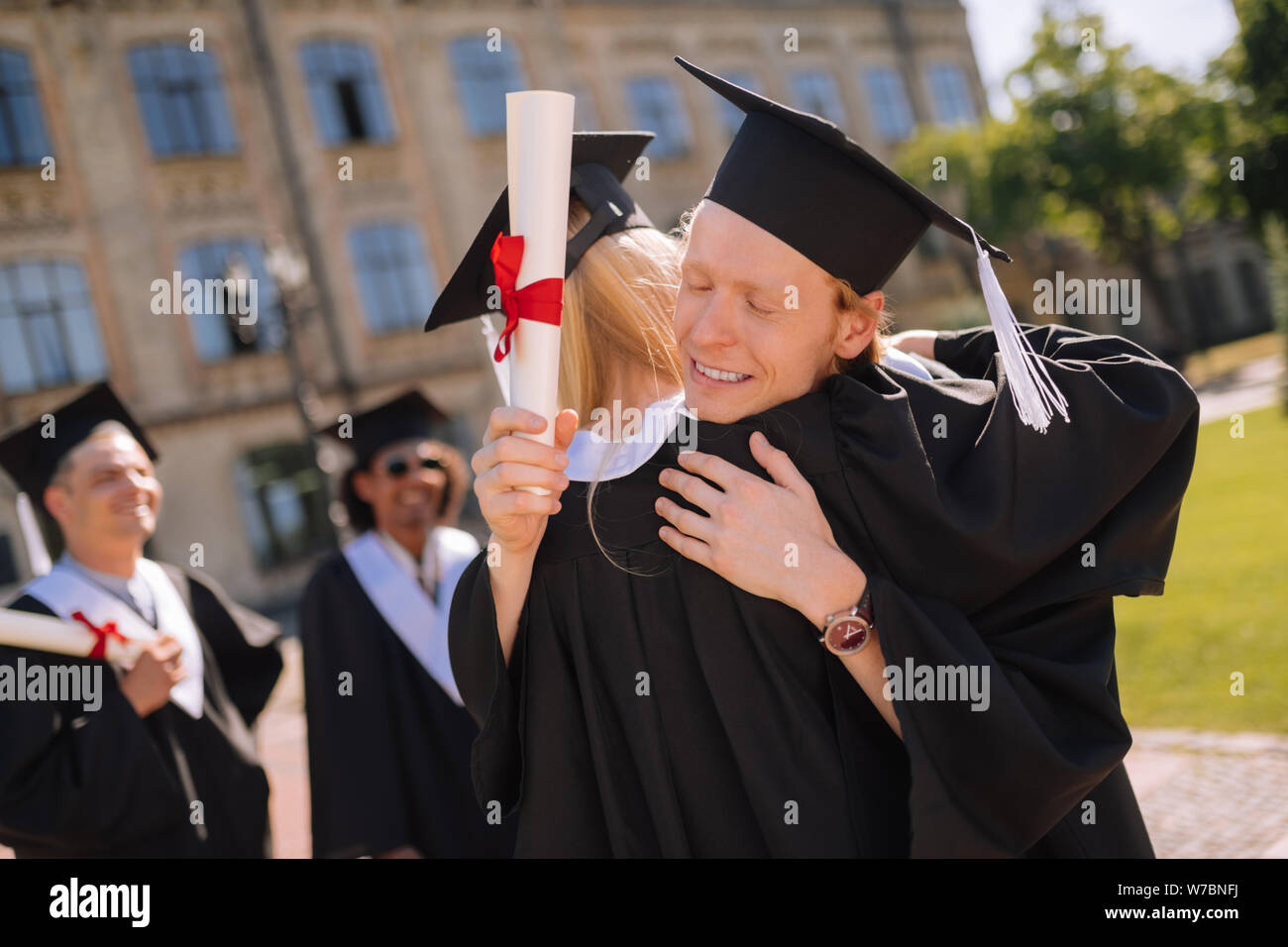 Two graduates hugging in front of their university. Stock Photo