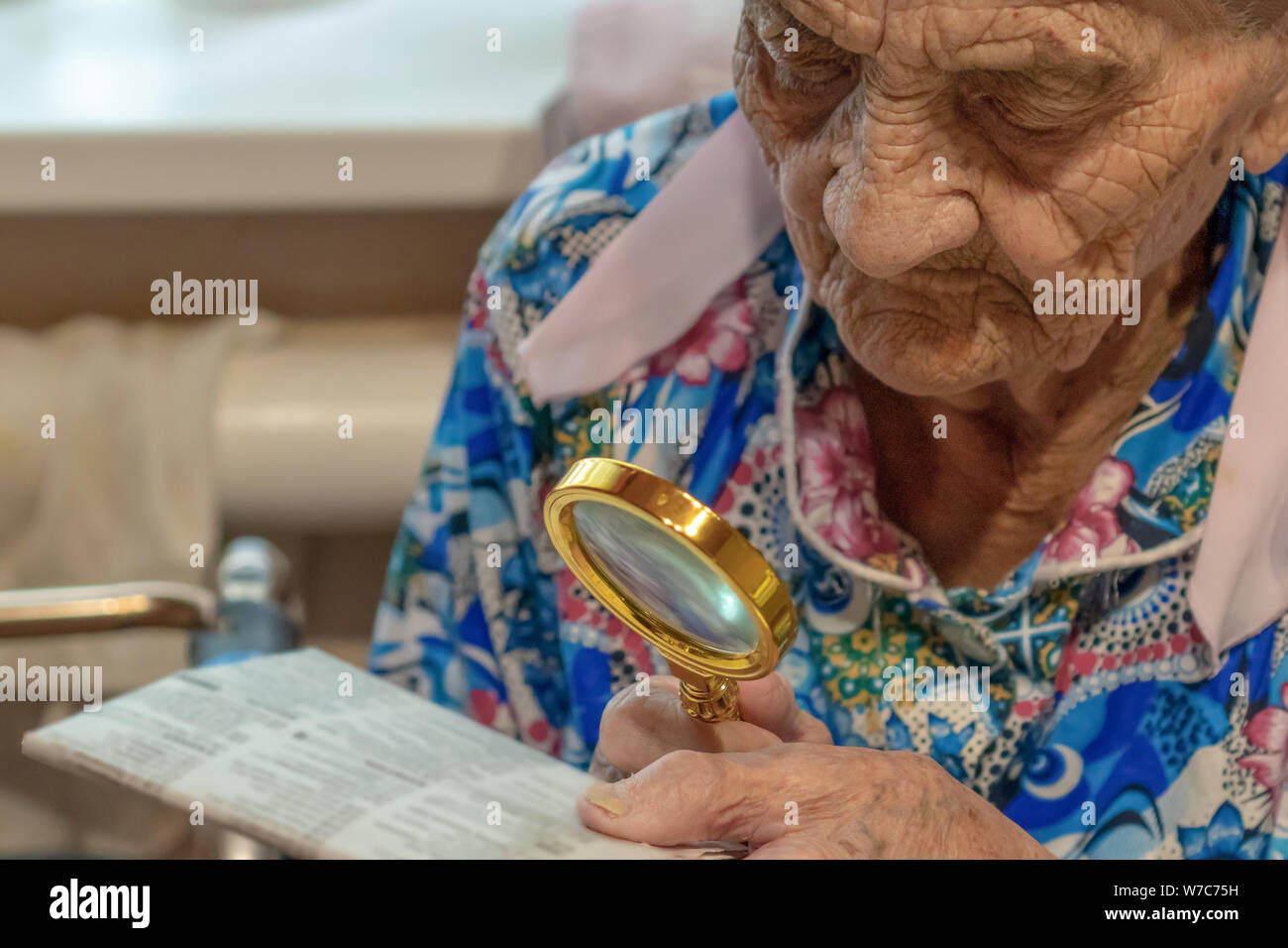 Very Old Woman with magnifier trying to Read from a newspaper. grandmother 90 years old reads at the table with magnifier . A close portrait. Stock Photo