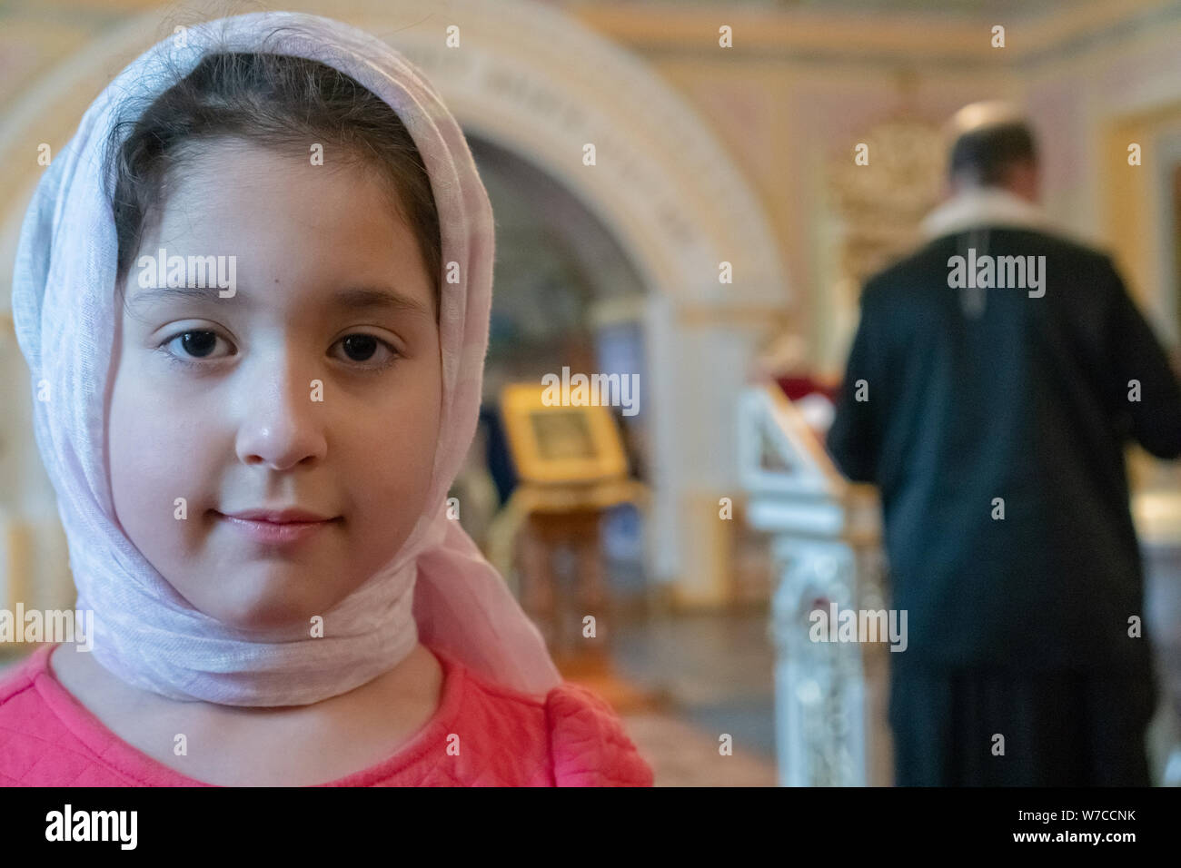 Teenager girl in a scarf in an orthodox temple. The priest reads ...