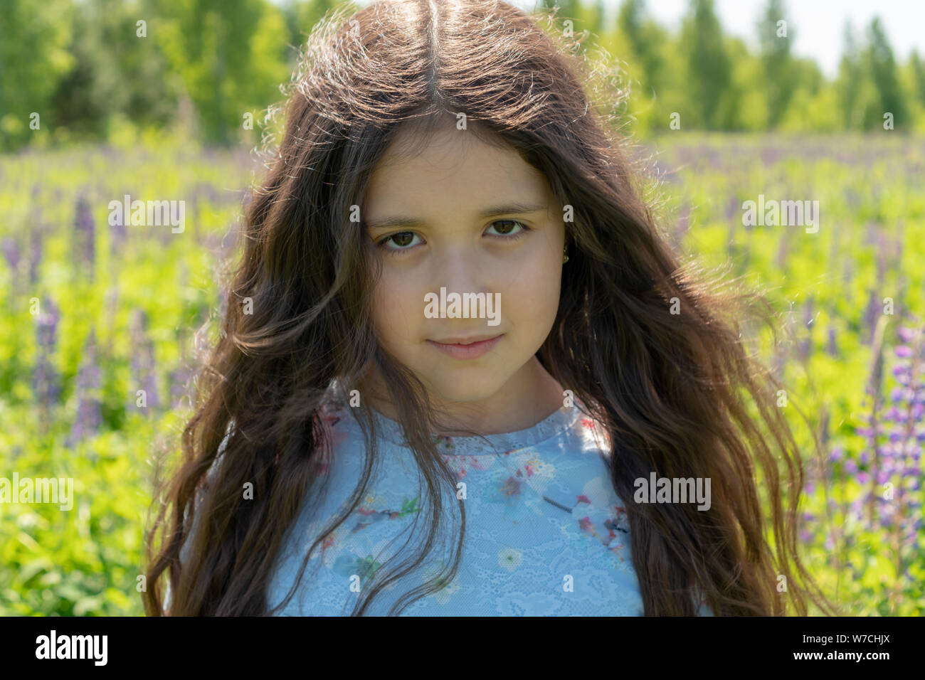 Portrait of a beautiful teenager girl with brown eyes and long, curly hair  on a field of flowers Stock Photo - Alamy