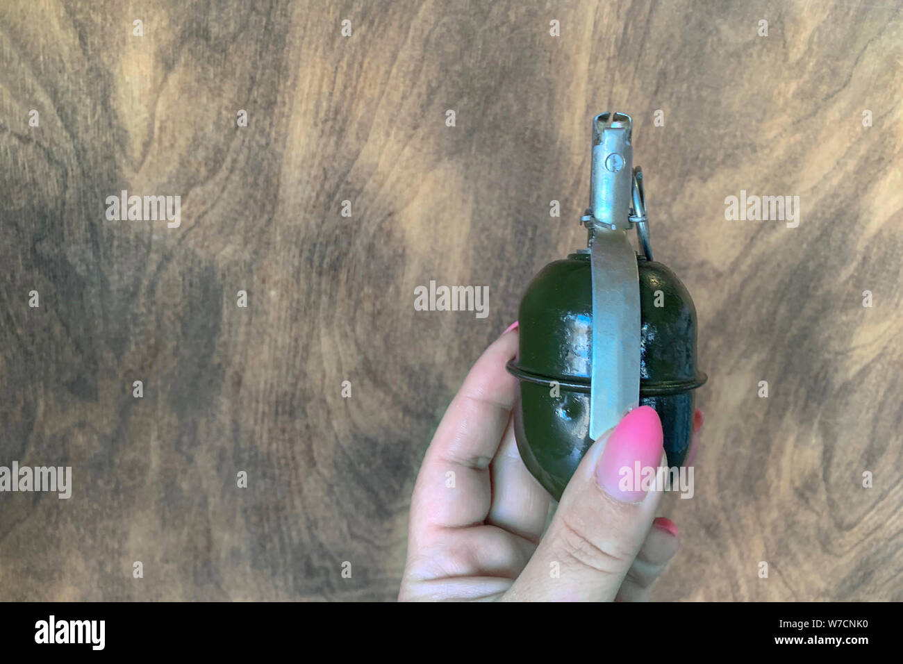 hand grenade in girl hand on wooden background. copy space Stock Photo