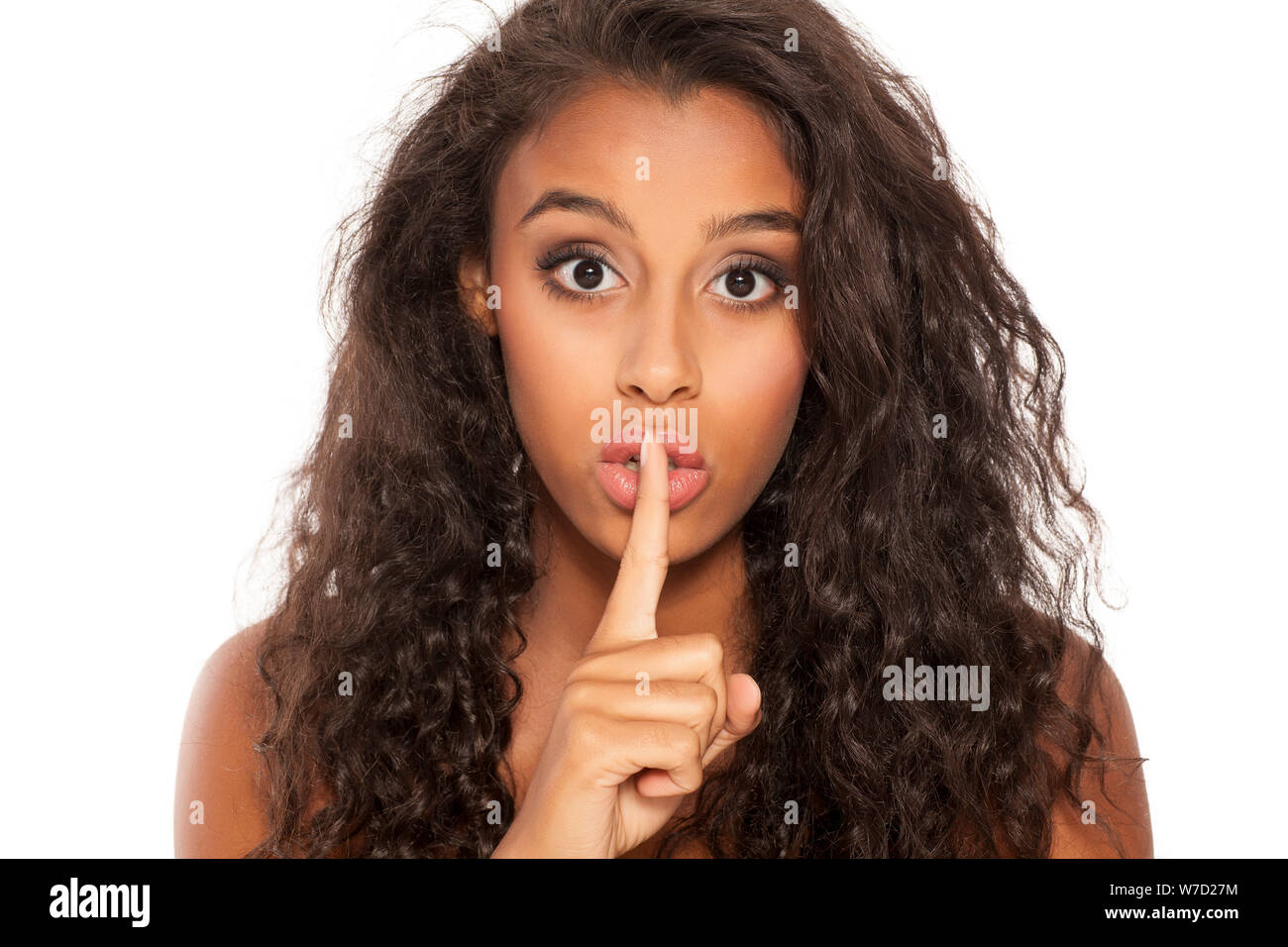 Portrait of a beautiful young dark-skinned woman with finger on her lips on a white background. Concept for silence Stock Photo
