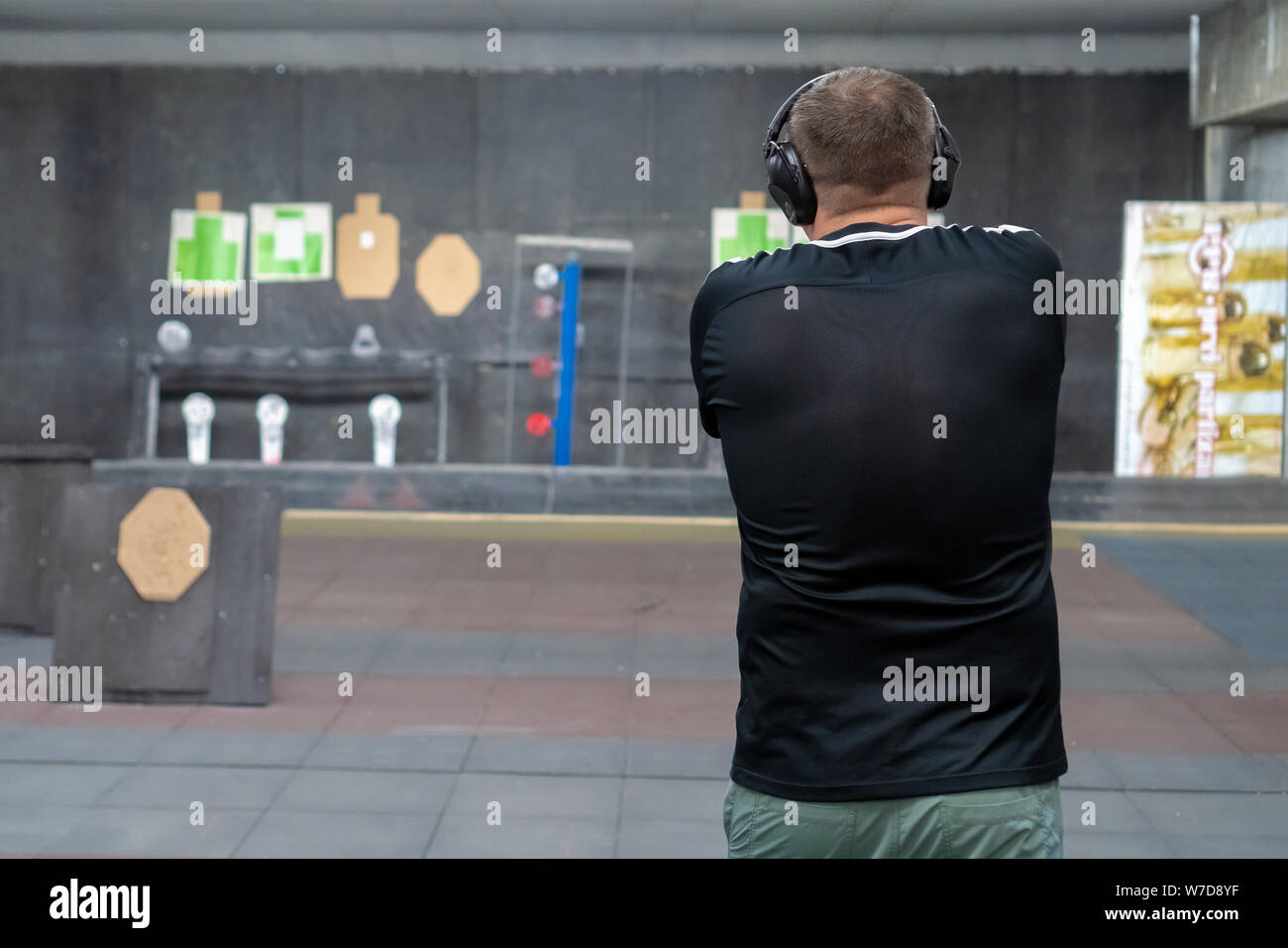 Man in shooting range in shooting action with GLOCK 19, view from behind o holding a pistol taking aim away from the camera with shallow depth of fiel Stock Photo