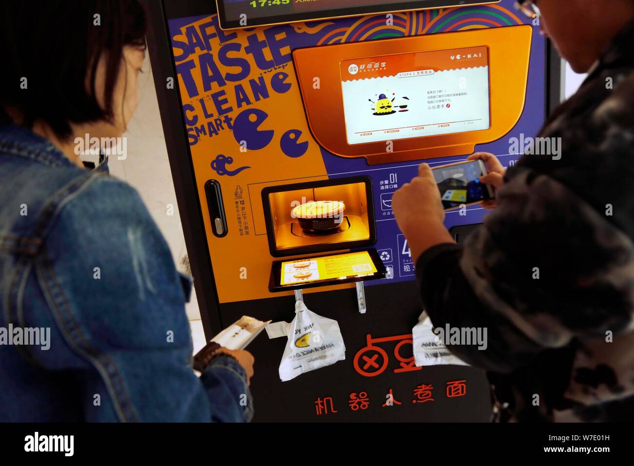 A customer takes photos of a bowl of noodle made by a mobile self-service noodle vending machine of Yo-Kai Express at an office building in Shanghai, Stock Photo