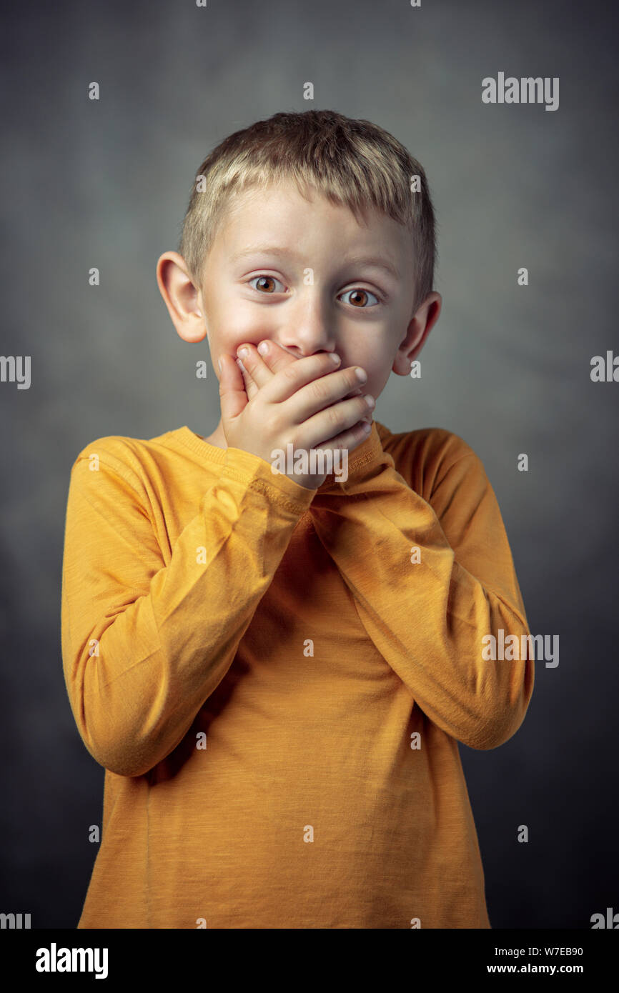 studio portrait of a 6 year old boy covering his mouth with both hands. Stock Photo