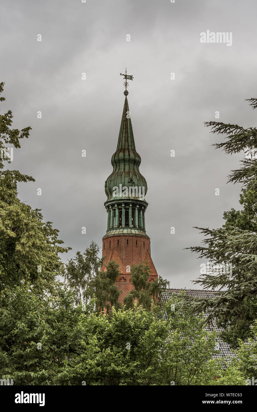 a copper spire on an onion dome among the green trees against a greyish sky at Frederiksvarek, Denmark, July 30, 2019 Stock Photo
