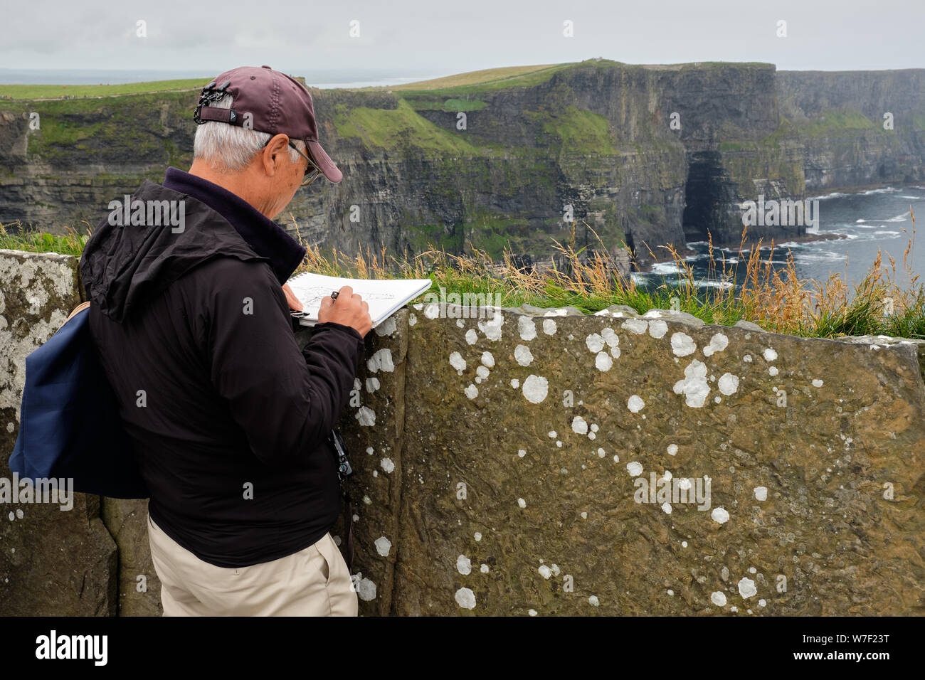 Tourist  sketching the scenery at the Cliffs of Moher on a grey rainy day Stock Photo