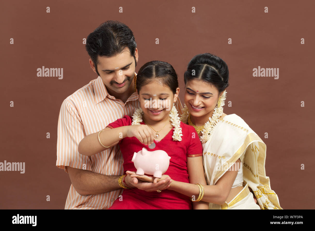 South Indian girl putting coin into a piggy bank with her parents Stock ...