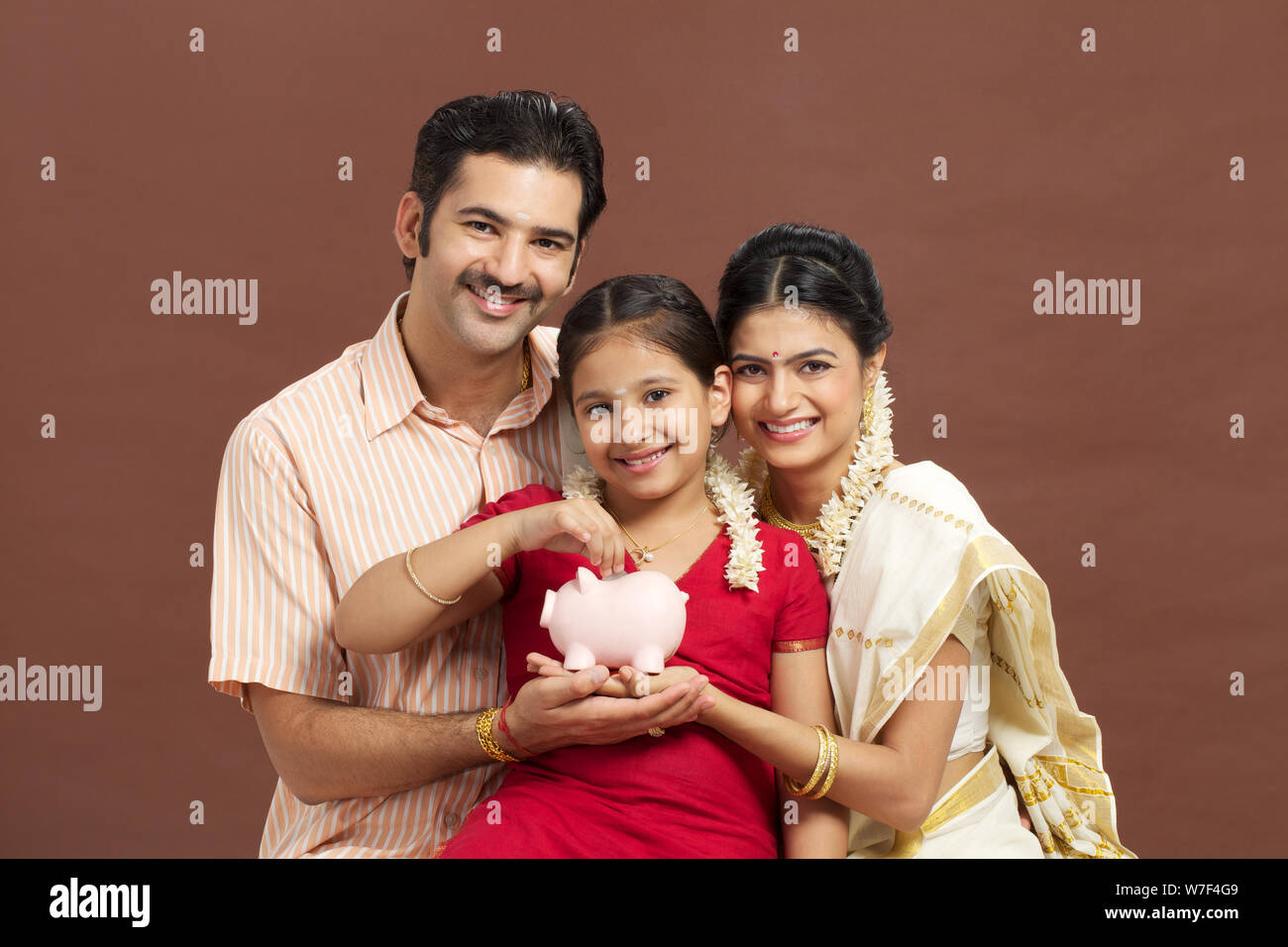 South Indian girl putting coin into a piggy bank with her parents Stock ...