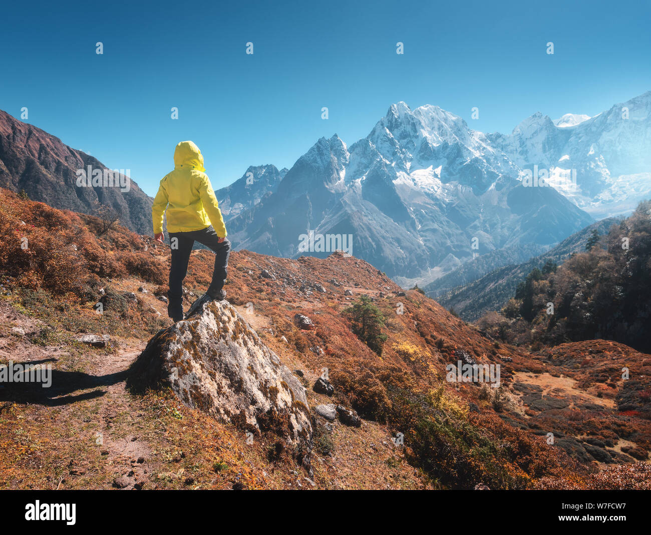 Sporty man on the stone is looking on snow covered mountains Stock Photo